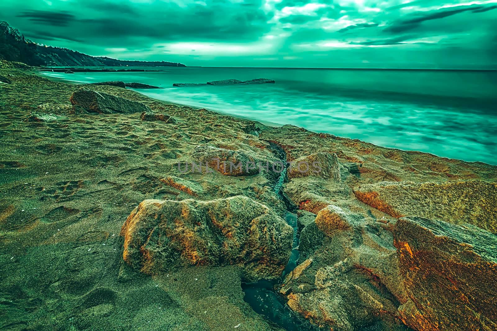 Creative view of cloudy sunrise with motion blur sea and rocks on the beach