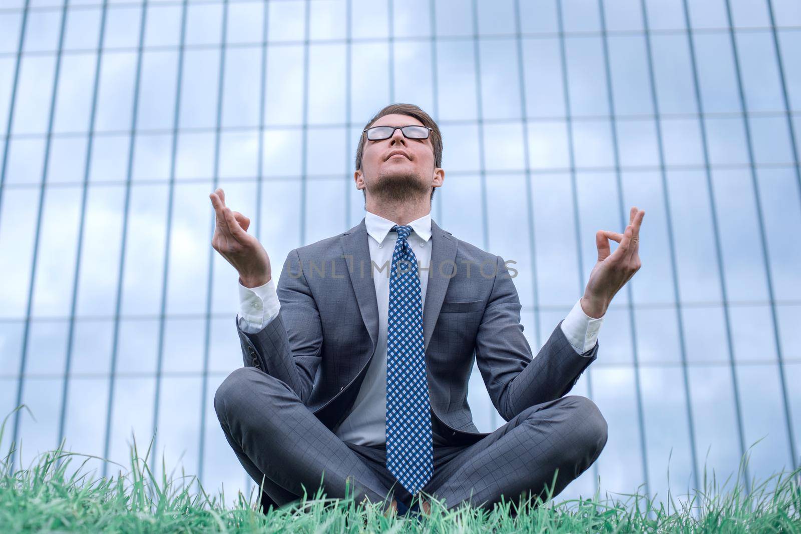 businessman in Lotus pose sitting on grass in front of office building by asdf