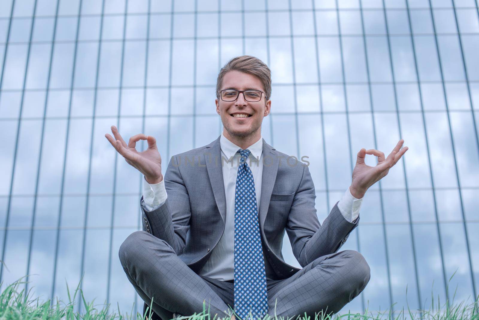 businessman in Lotus pose sitting on grass in front of office building. photo with copy space