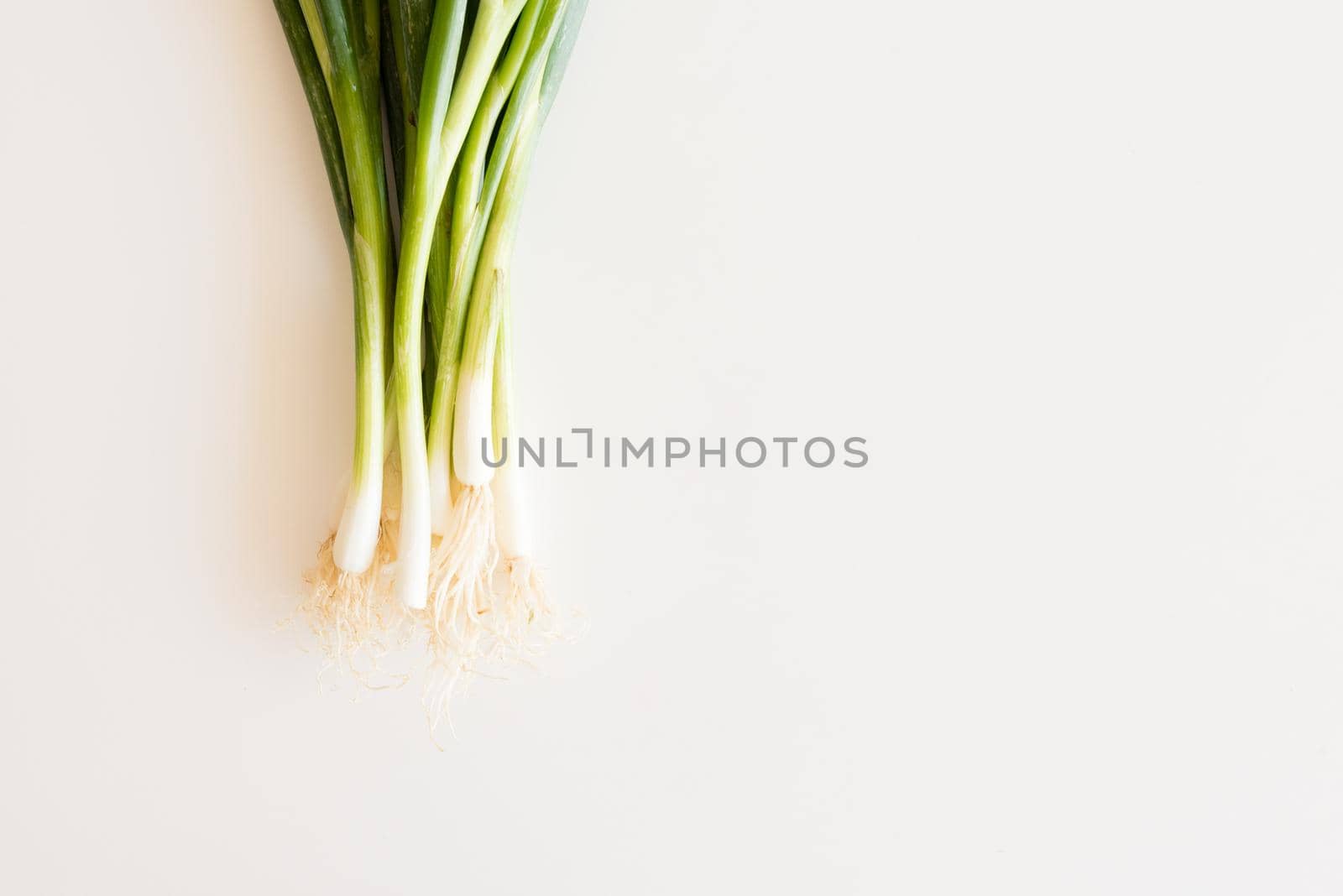 Cropped view of spring onions on white table from above with copy space to right by natalie_board