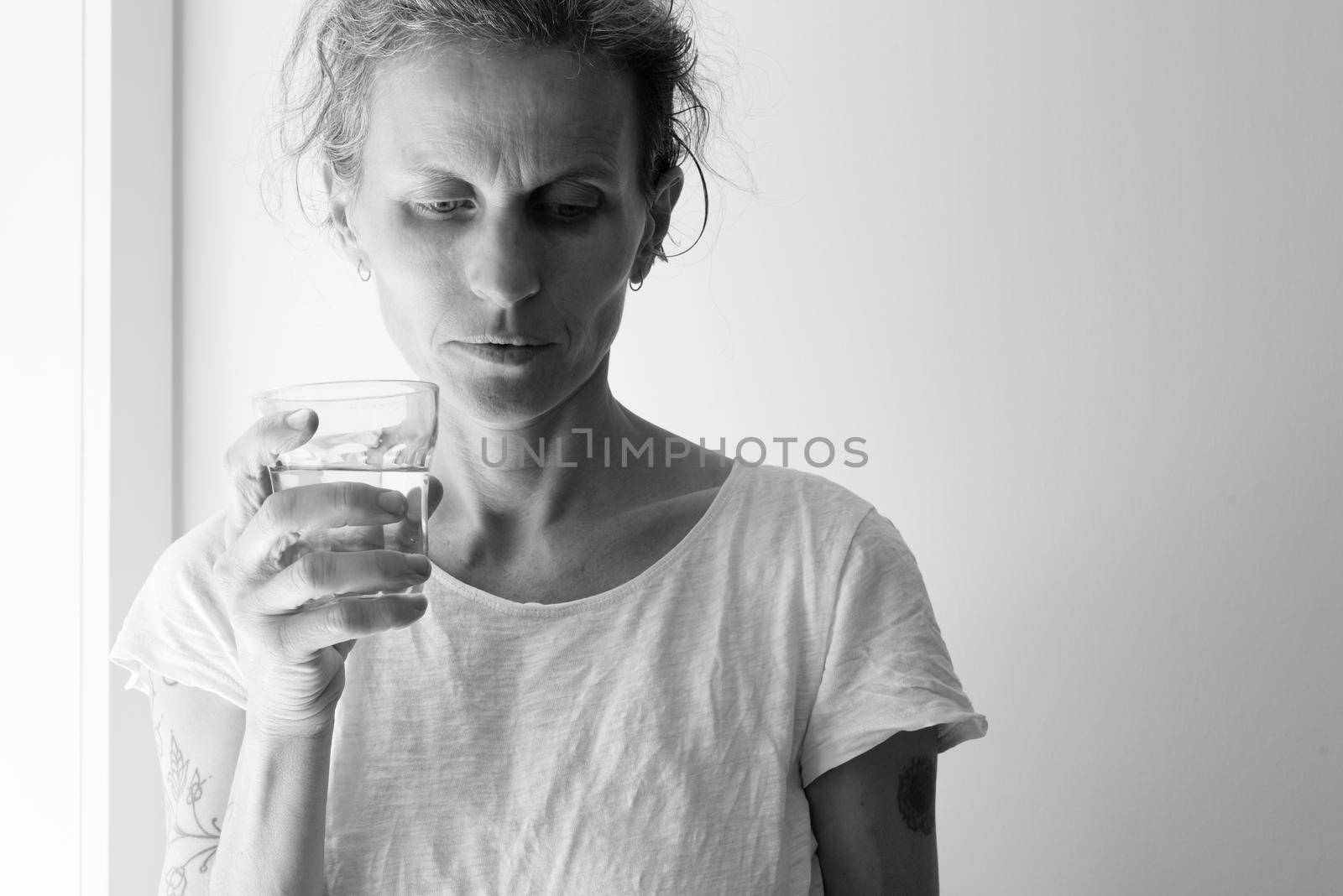 Middle aged woman holding glass and looking pensive - addiction concept (black and white) by natalie_board