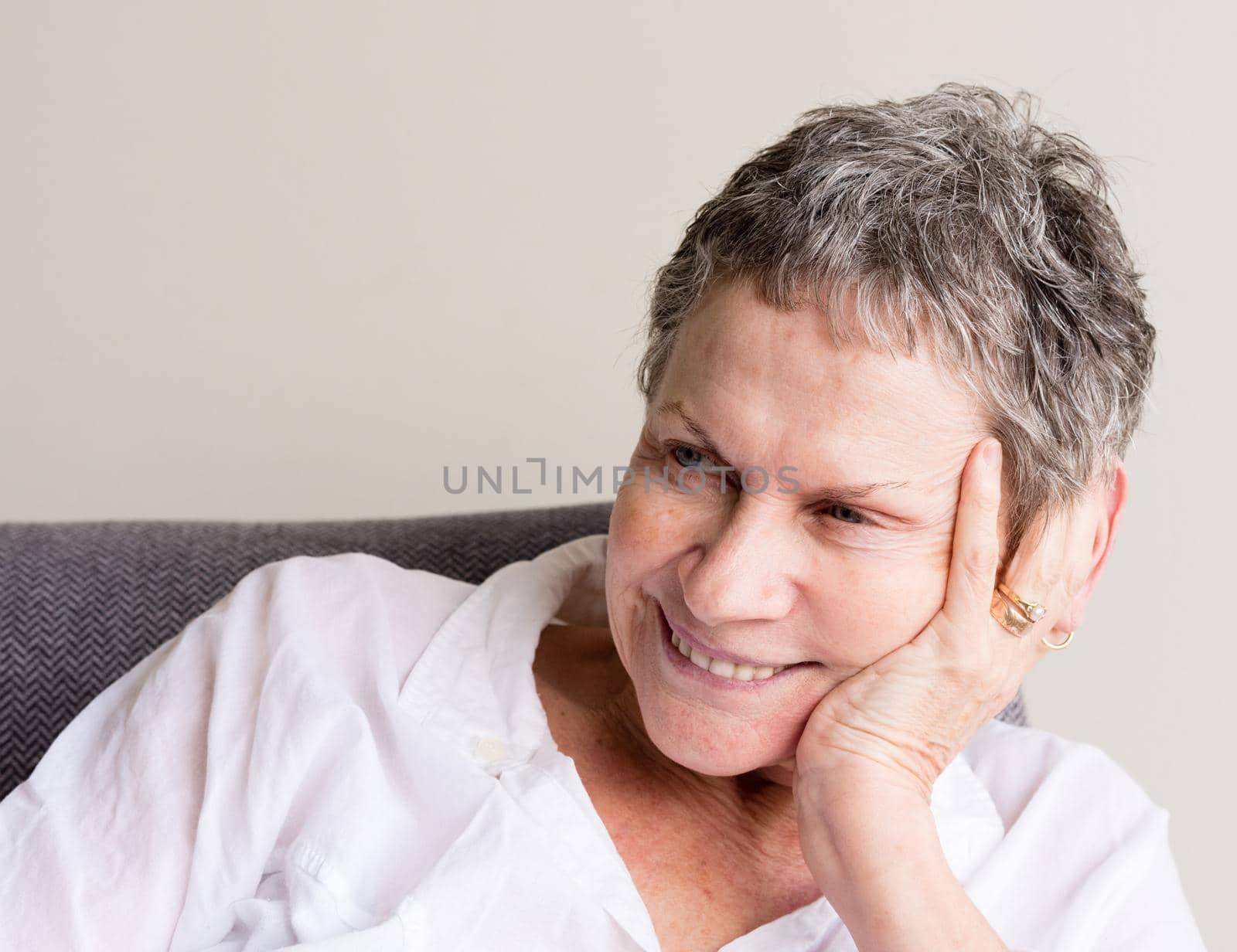 Older woman with short grey hair smiling with hand on head in relaxed position (selective focus) by natalie_board