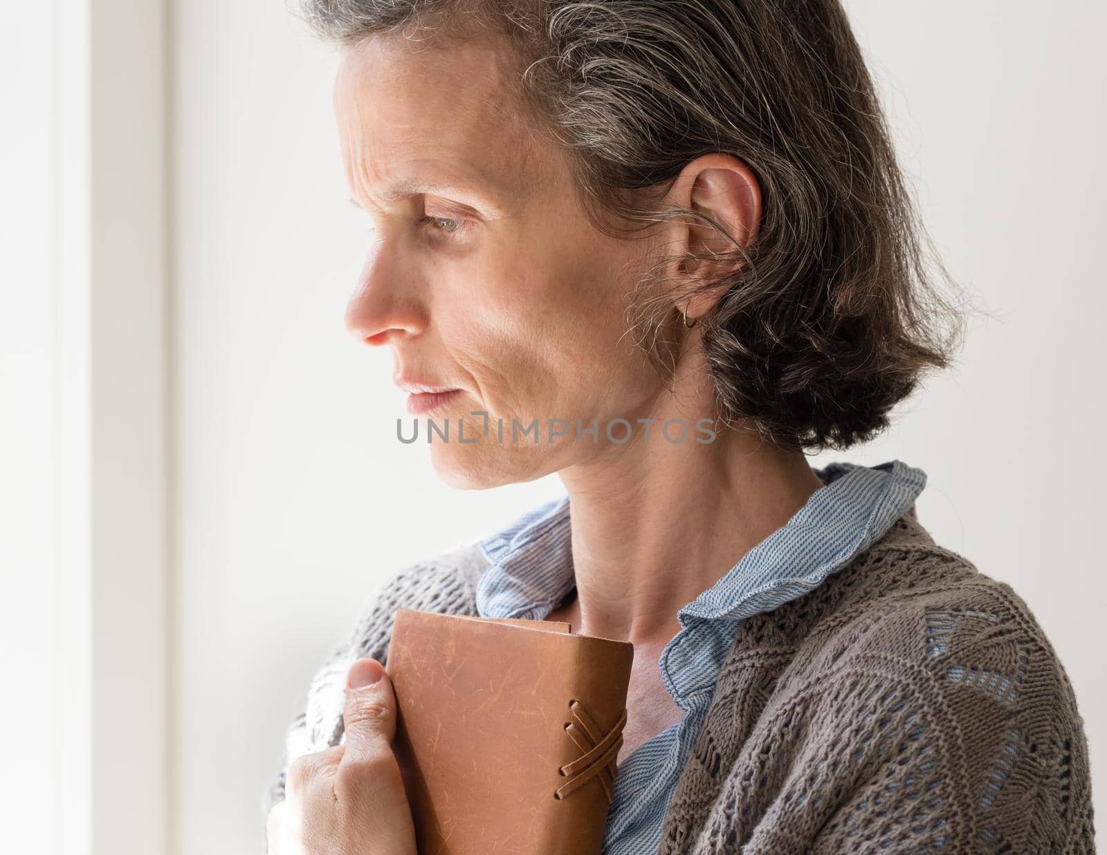 Profile view of middle aged woman with grey hair frowning and holding book (selective focus)