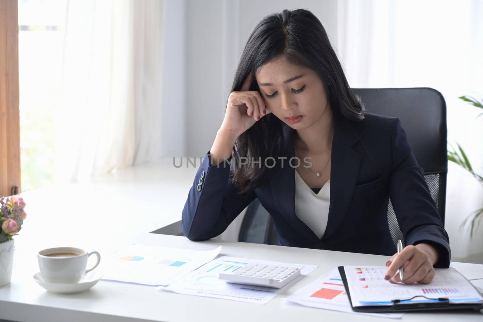 Serious female accountant sitting at her workplace and checking financial document.