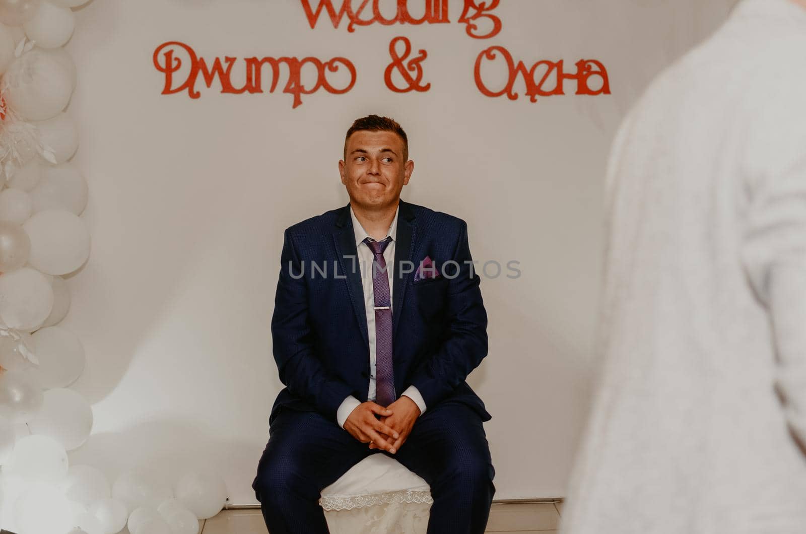 a man in a suit sitting on a chair puzzled. the groom the husband sits and waits for the bride. young man experiences strange emotions on face. Slavic Ukrainian Russian wedding traditions