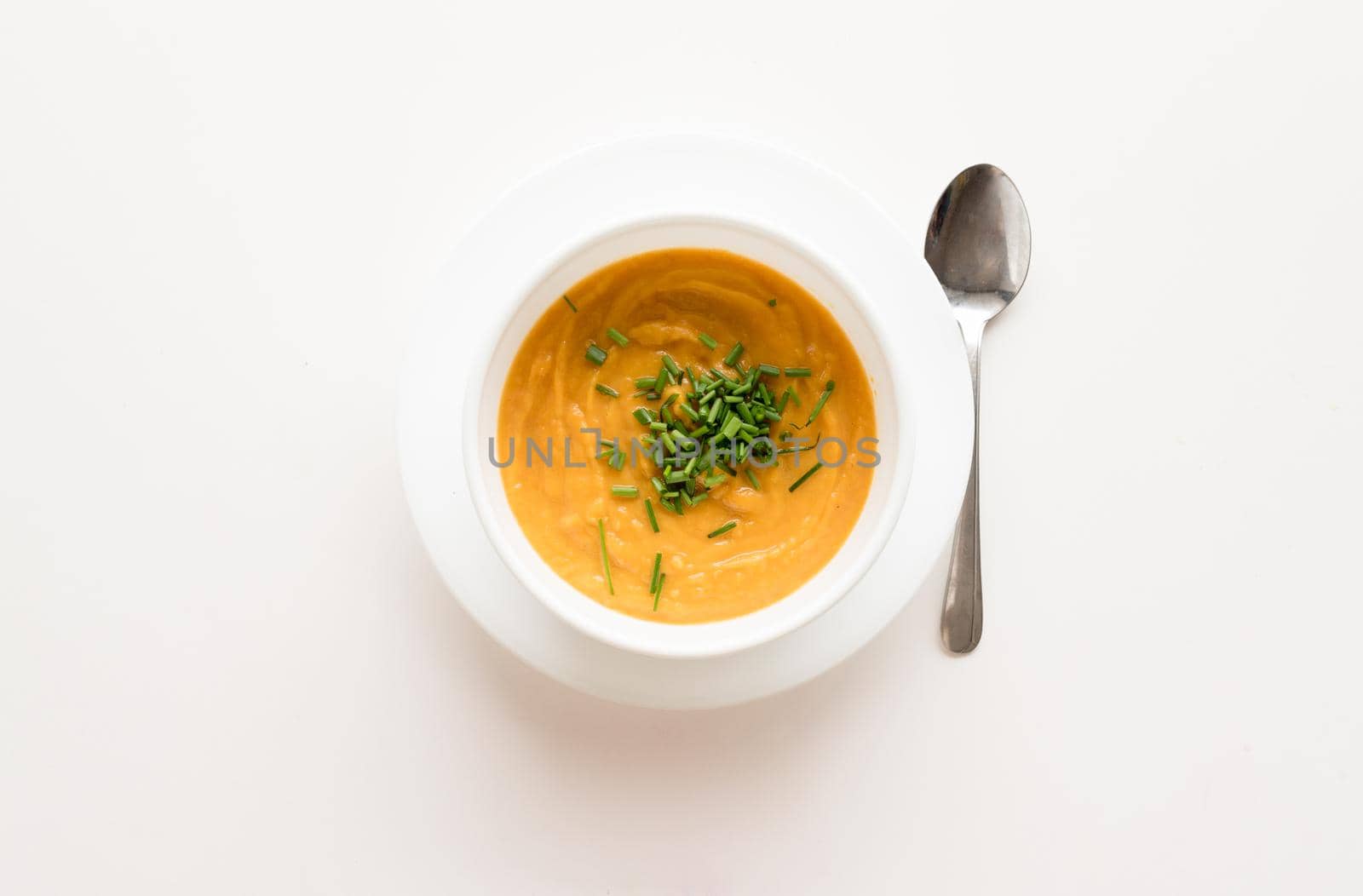High angle view of roasted root vegetable soup with sprinkled chives in white bowl on table with spoon
