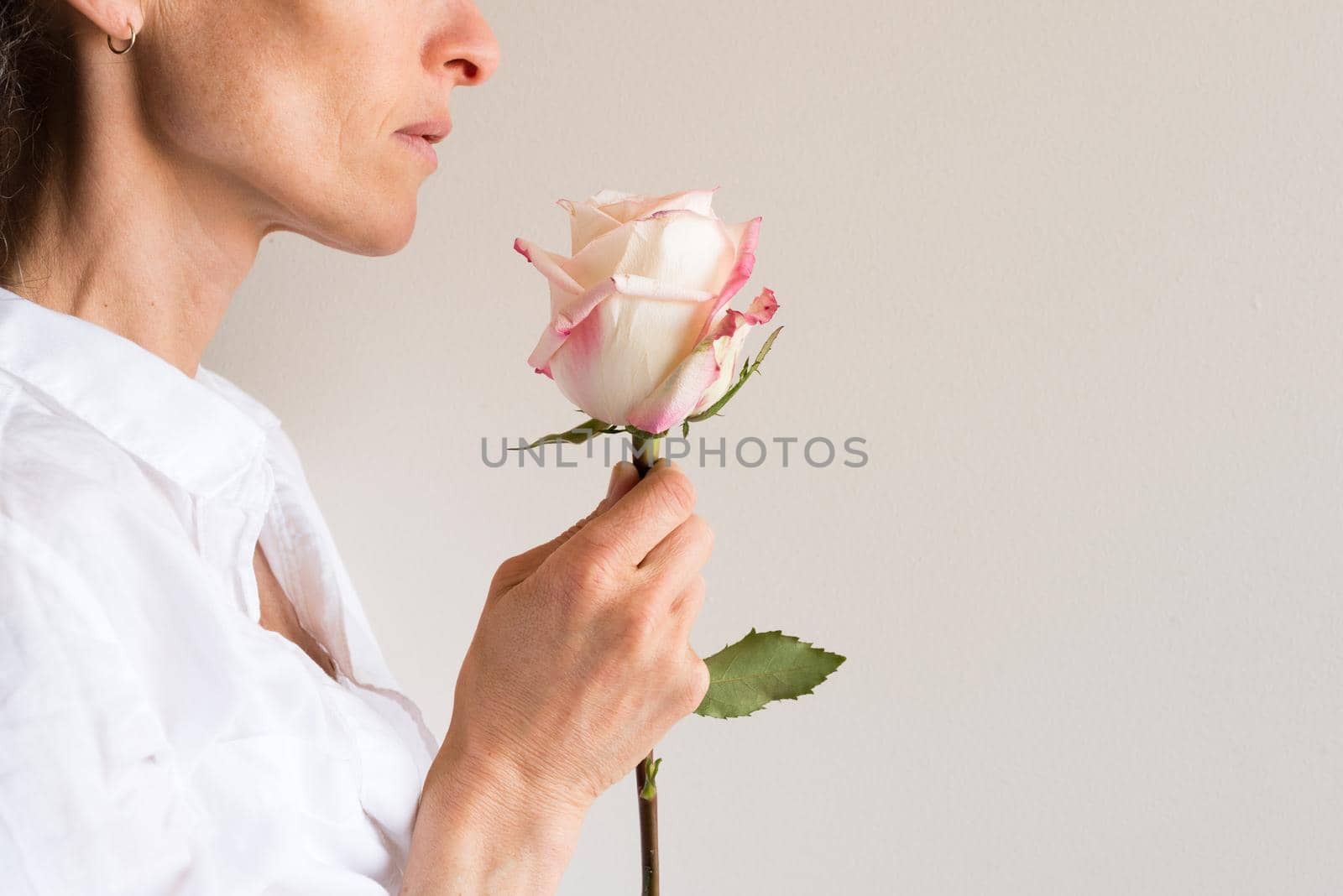 Profile view of middle aged woman holding single pink and cream rose (cropped)