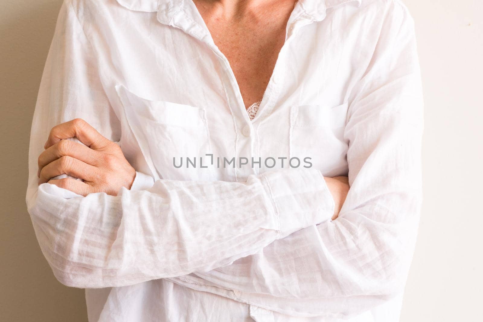 Faceless view of middle aged woman in white shirt with arms crossed against neutral background (cropped)