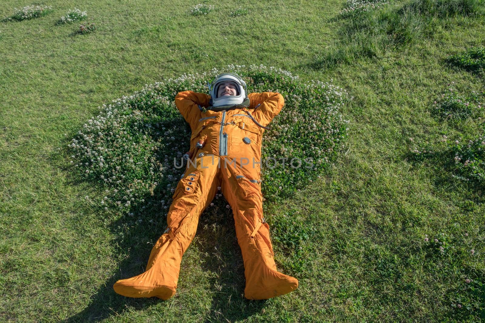Happy cosmonaut wearing space suit and helmet having a rest while lying on green grass outdoor by dmitryz