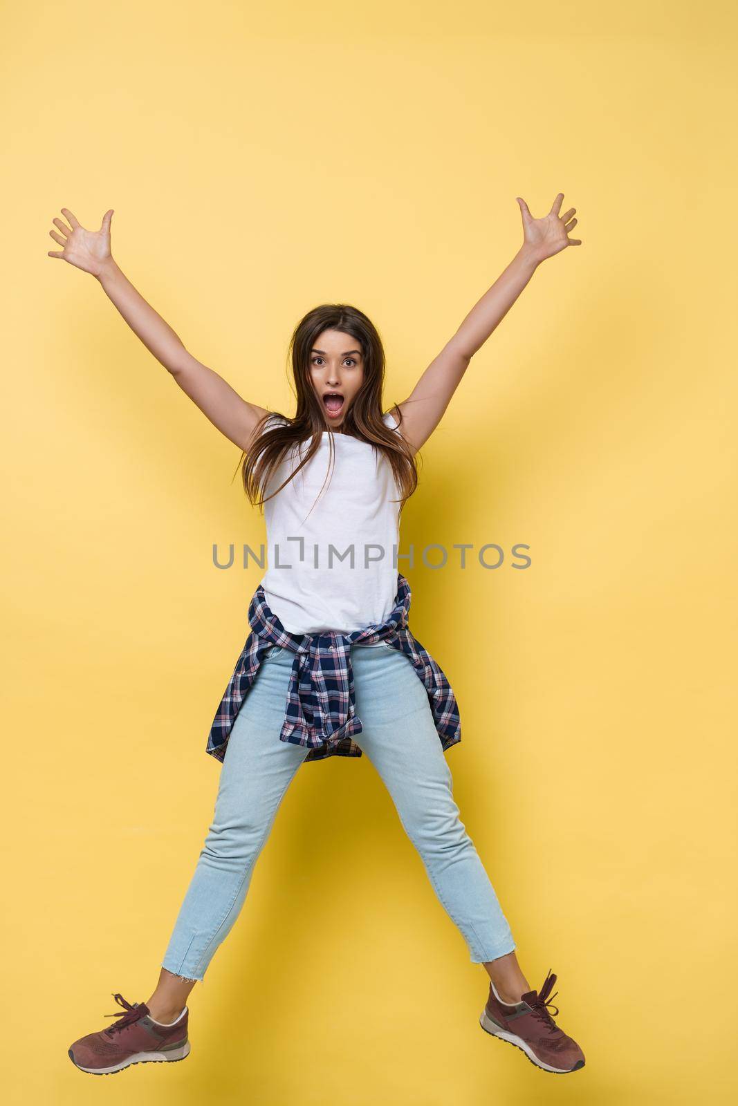 Full length portrait of a cheerful casual caucasian woman jumping isolated over yellow background.