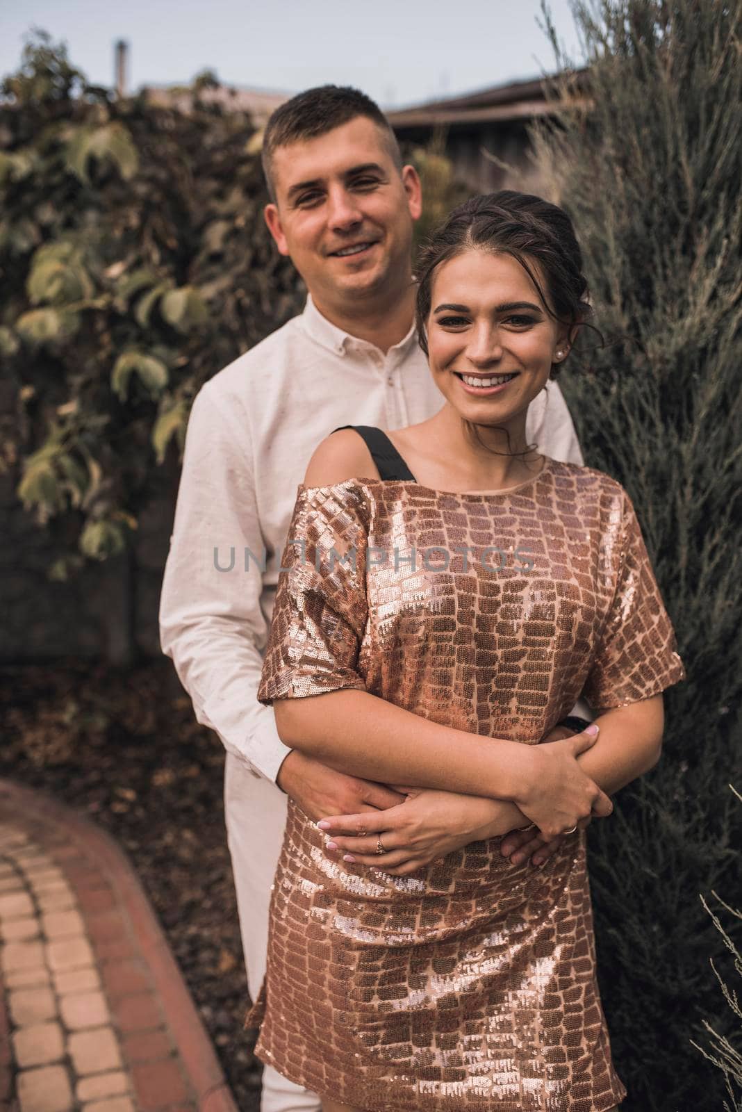 Young couple of lovers man and woman in festive fashionable clothes are hugging. Light casual hairstyle for women with a perm. Summer nature outside background.