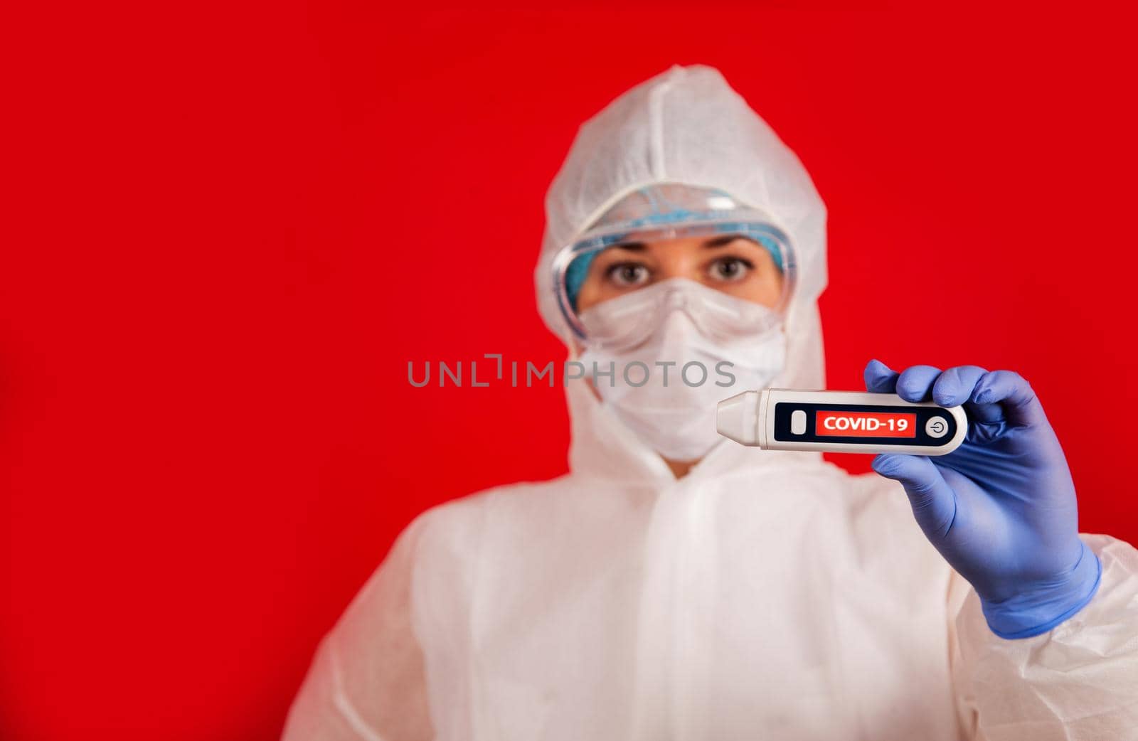 Coronavirus. The New Coronavirus COVID-19, Wuhan, China. A woman in a mask on a red background with a coronavirus reads its temperature on a thermometer with the inscription COVID-19.