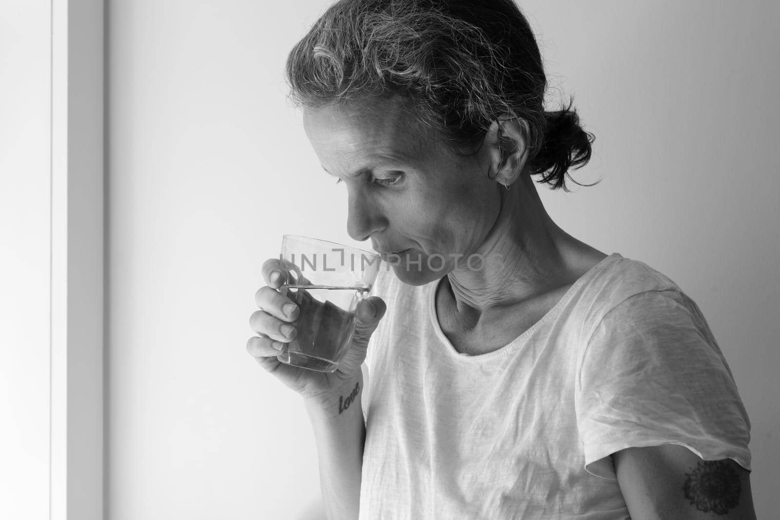 Profile of middle aged woman holding glass and looking pensive - addition concept (black and white)