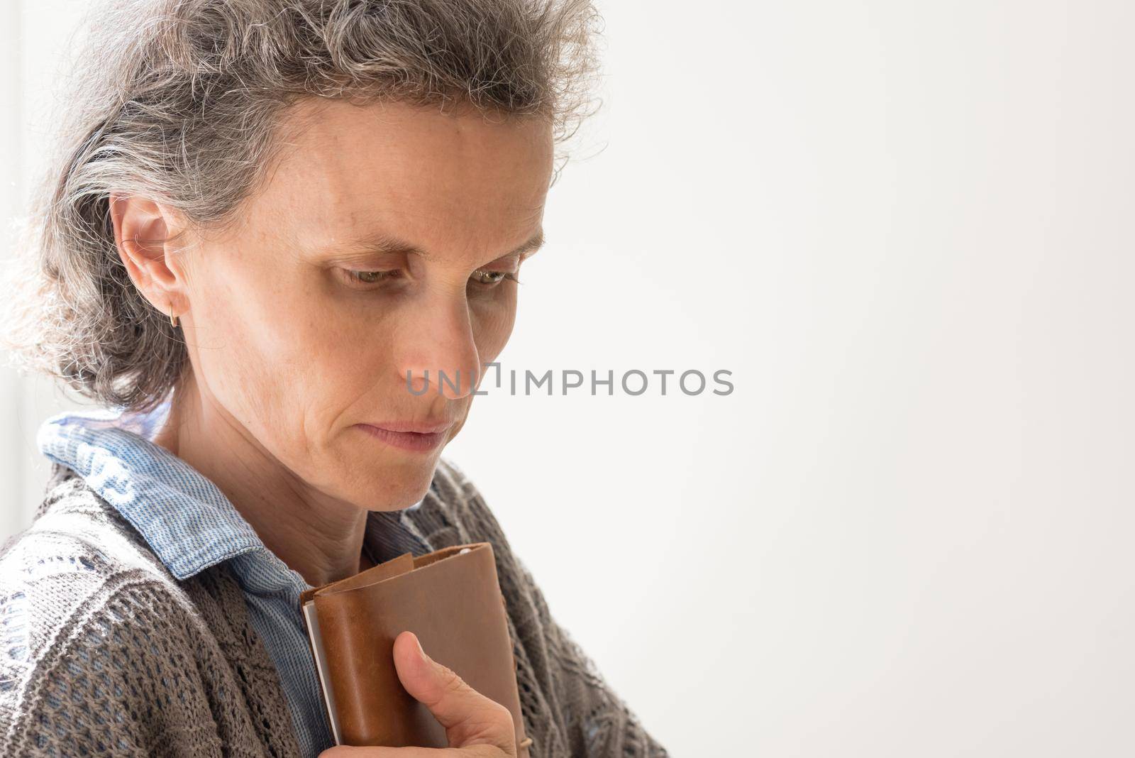 Middle aged woman with grey hair looking tired and anxious and holding book (selective focus) by natalie_board