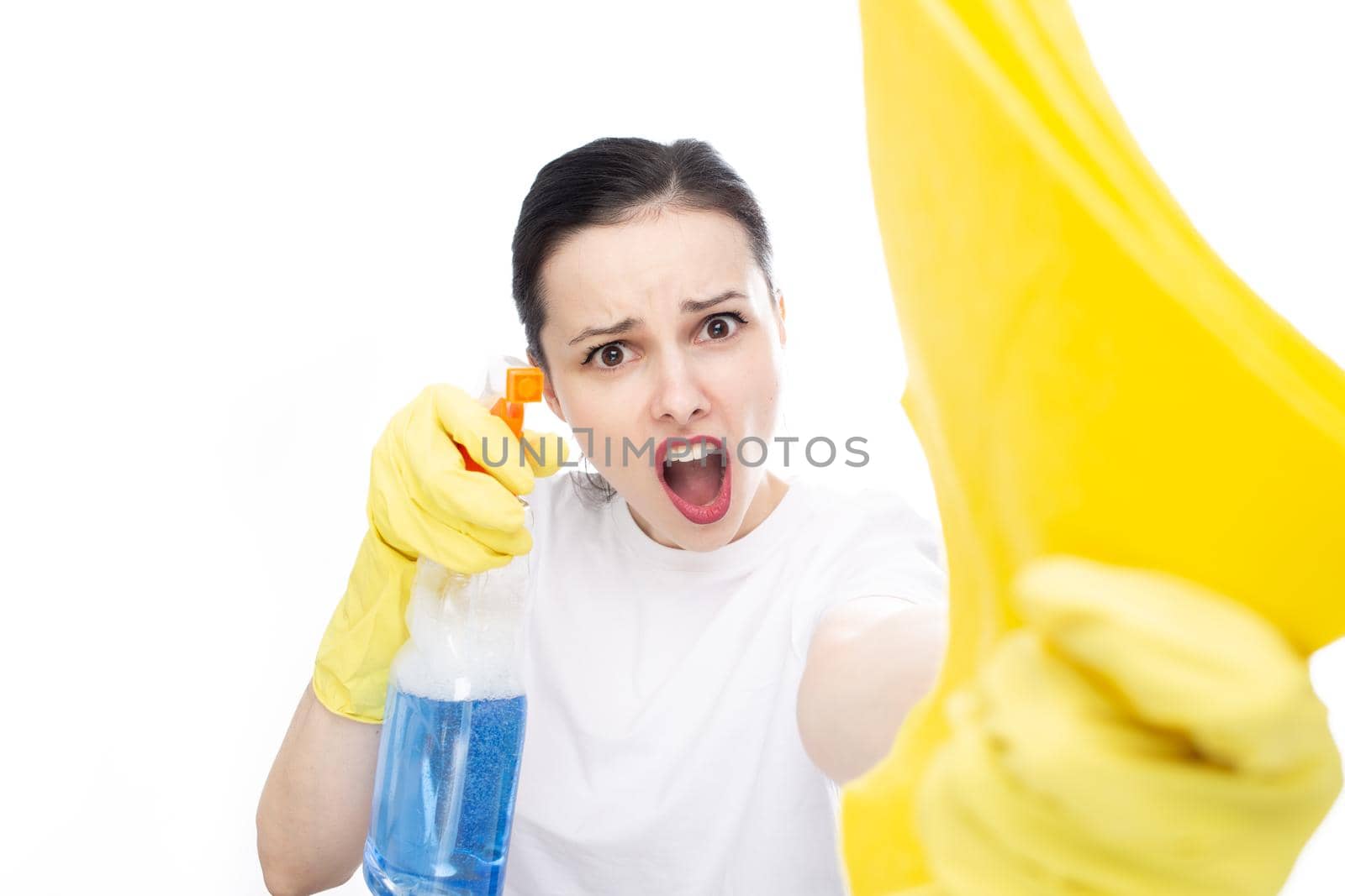 funny woman in yellow gloves holds rags and cleaning agent in her hands, white studio background. High quality photo