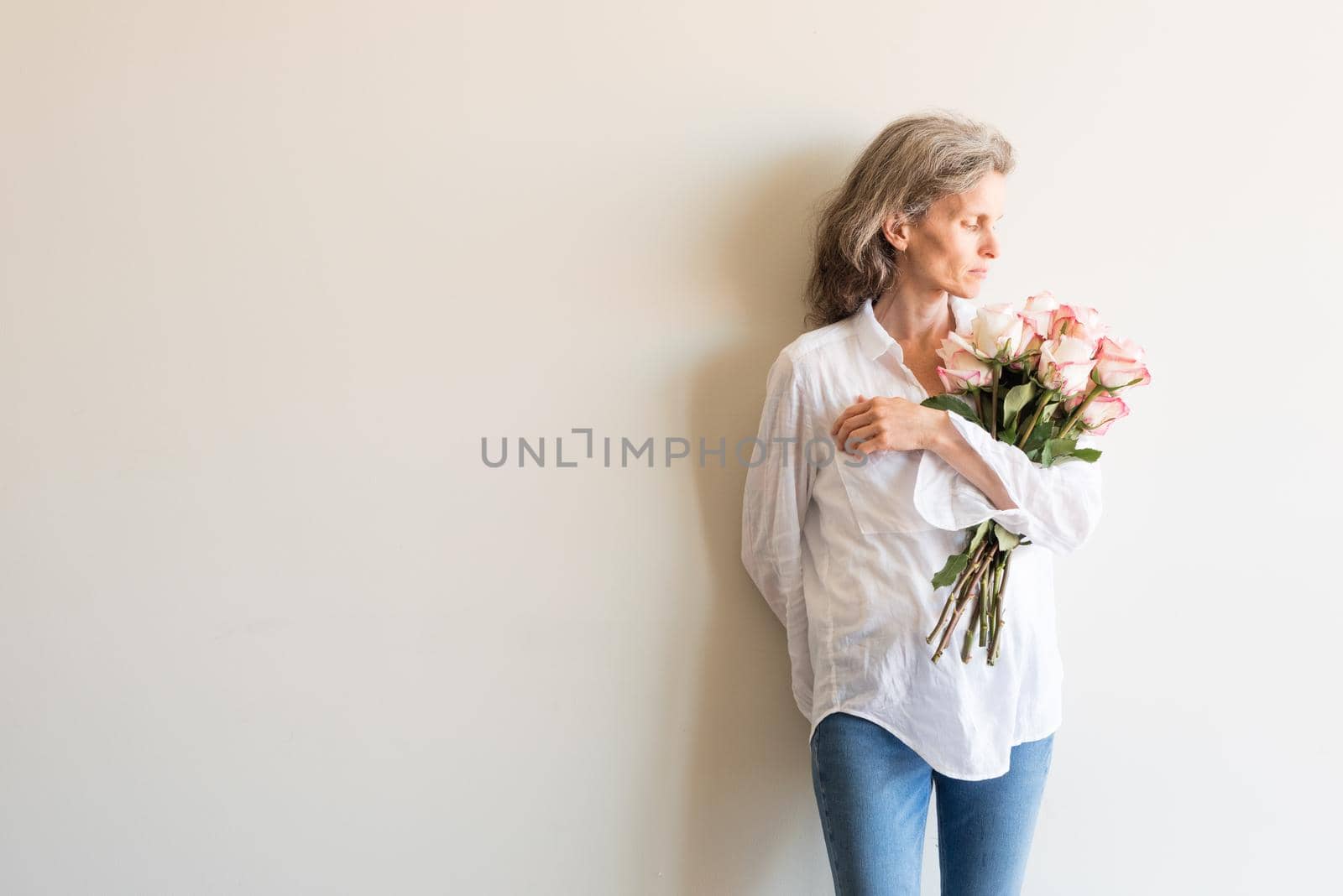 Half length view of middle aged woman with grey hair and white shirt holding pink and cream roses by natalie_board