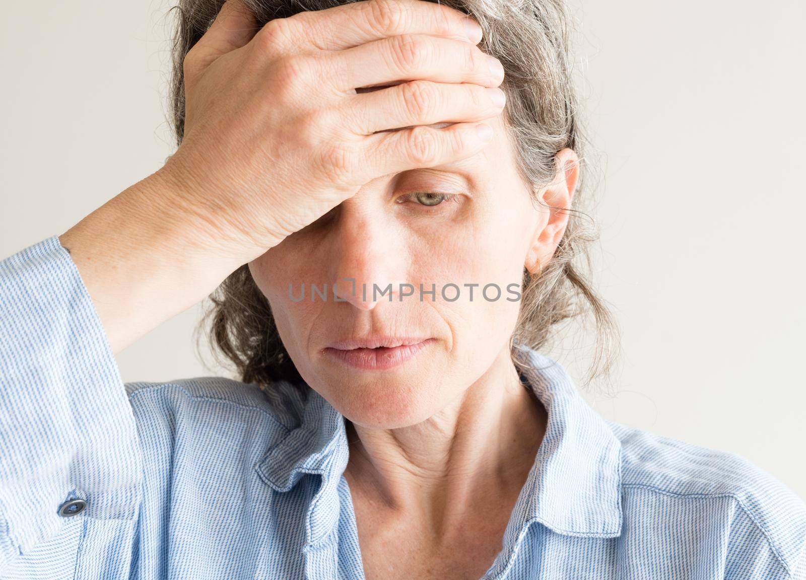 Close up of middle aged woman with hand on forehead covering one eye by natalie_board