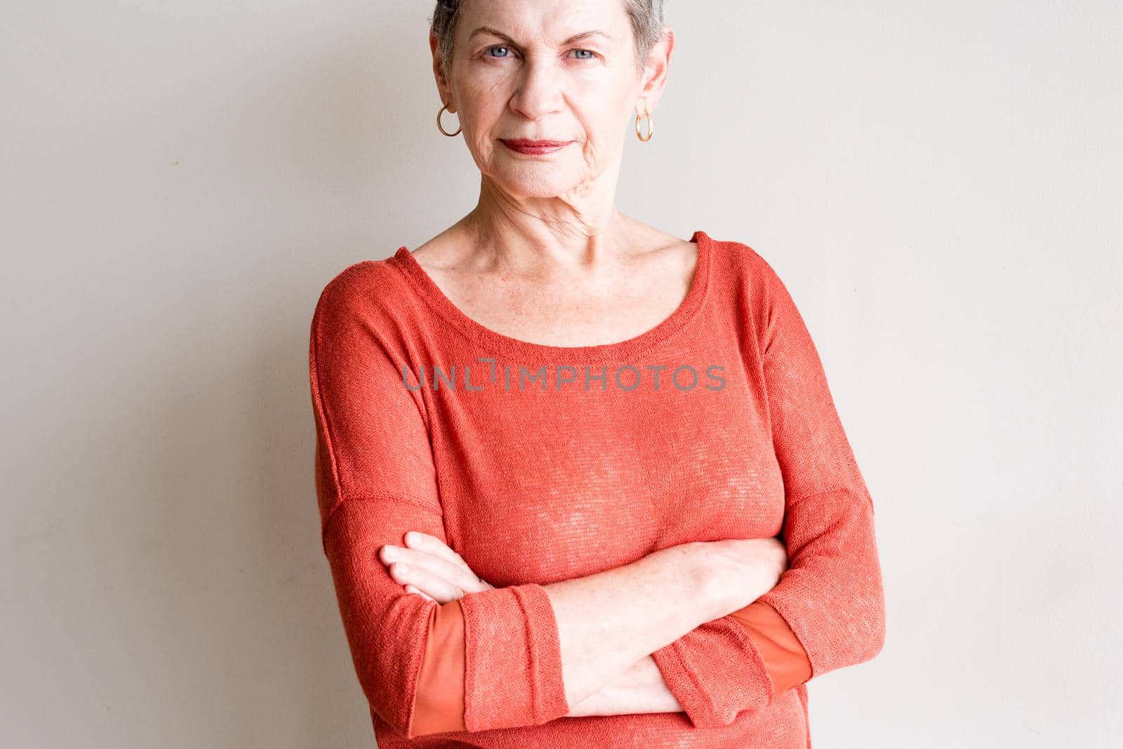 Older woman with short grey hair and orange top with arms crossed