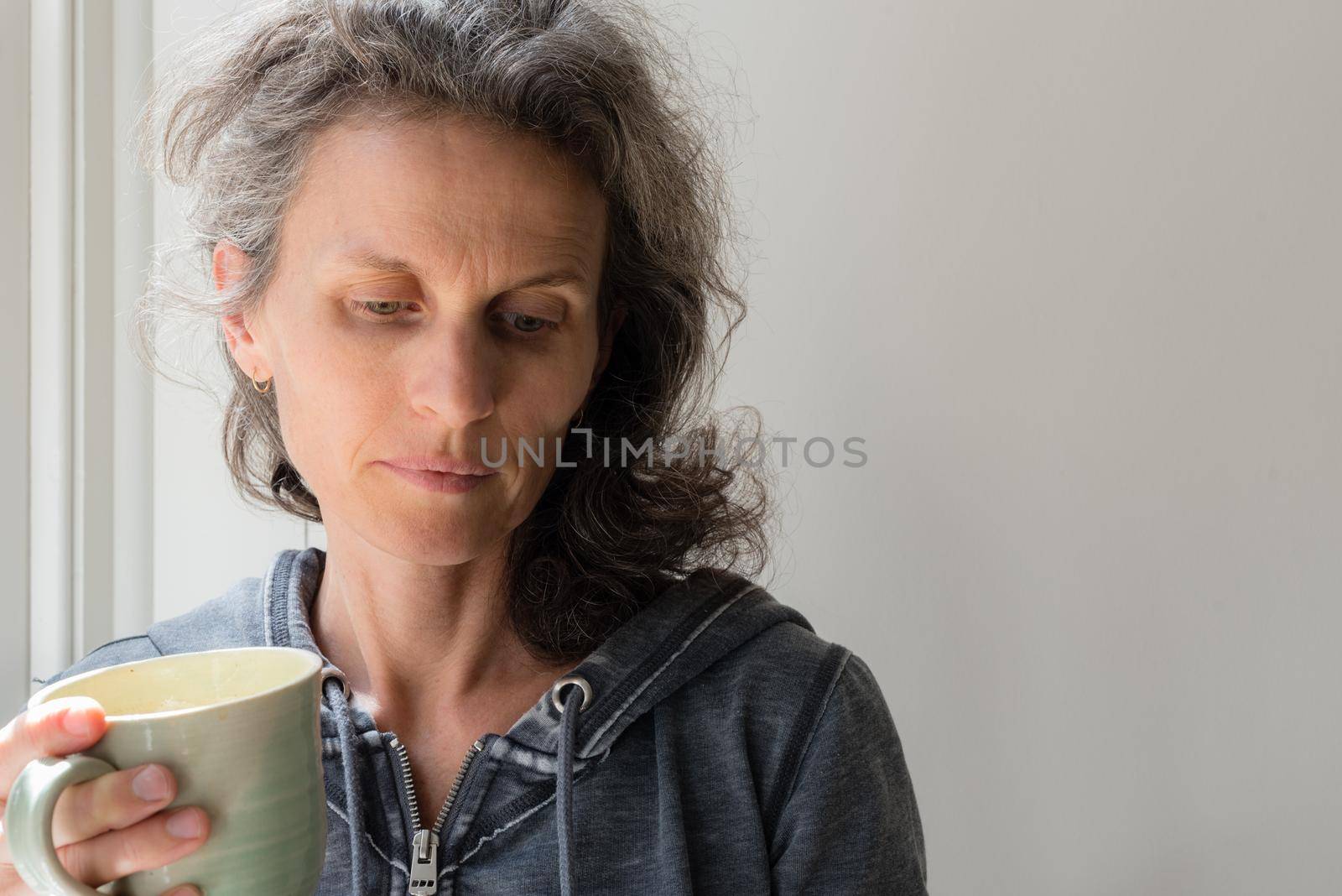 Middle aged woman with grey hair holding green cup and looking pensive (selective focus) by natalie_board
