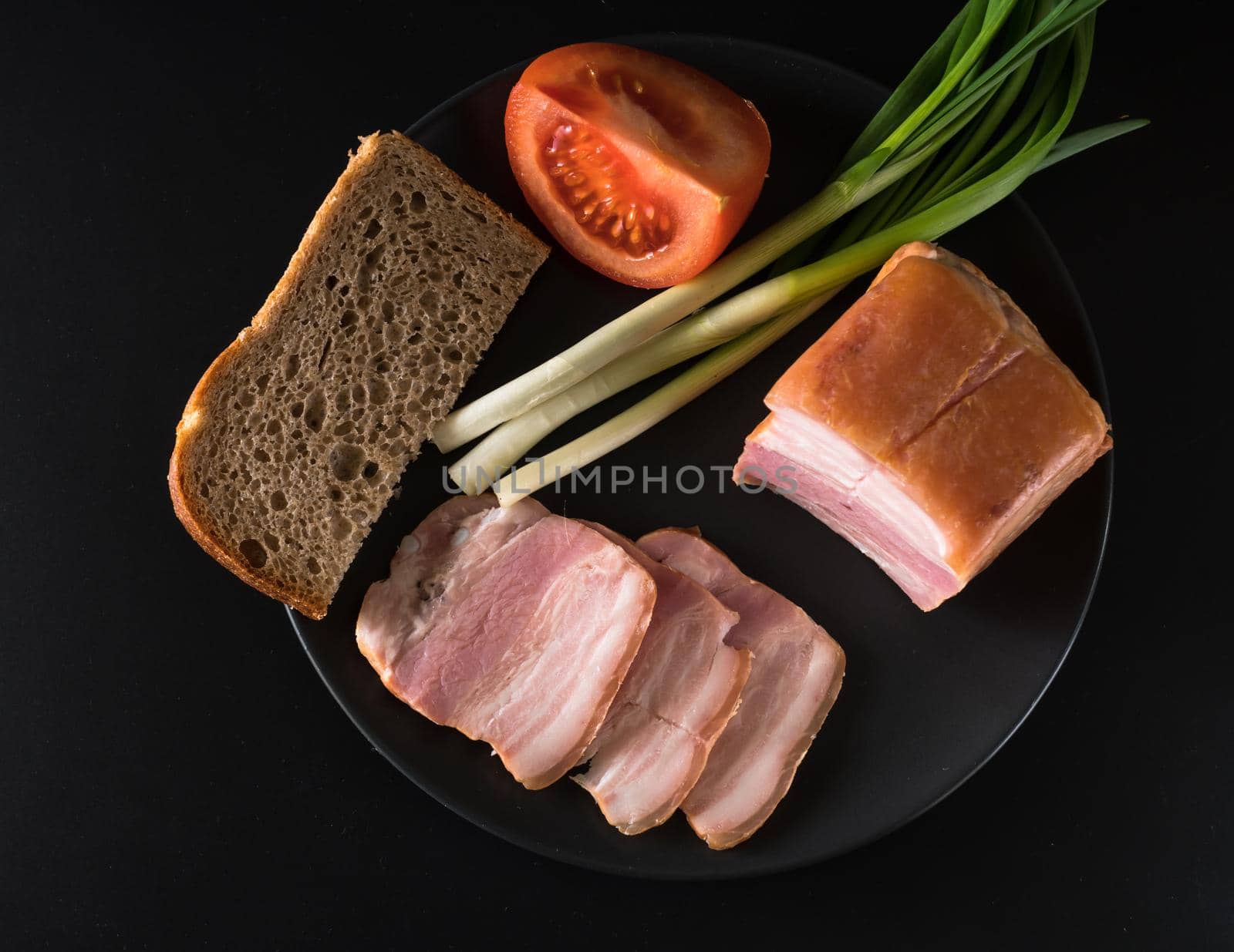 Food, lard, green onions, tomato, black bread, on a black plate, on a black background
