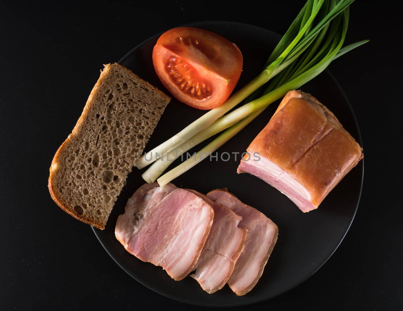 Food, lard, green onions, tomato, black bread, on a black plate, on a black background