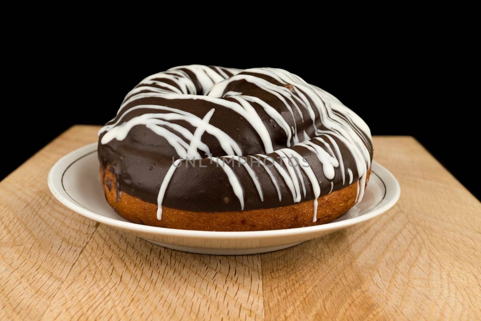 bun covered with chocolate, in a white plate, on a wooden board, on a black background, close-up