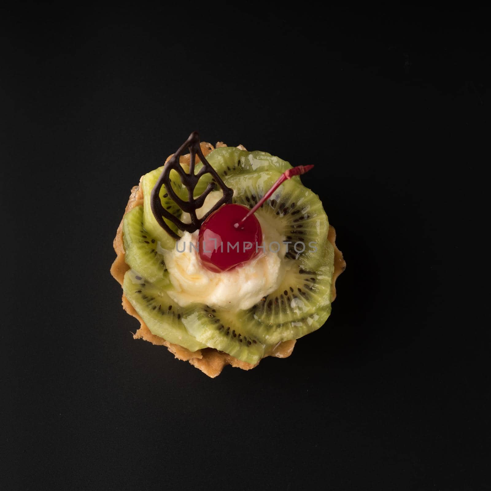 Fruit dessert cake with cherries, shecolade leaf, kiwi wedges and protein cream, on a black background isolated