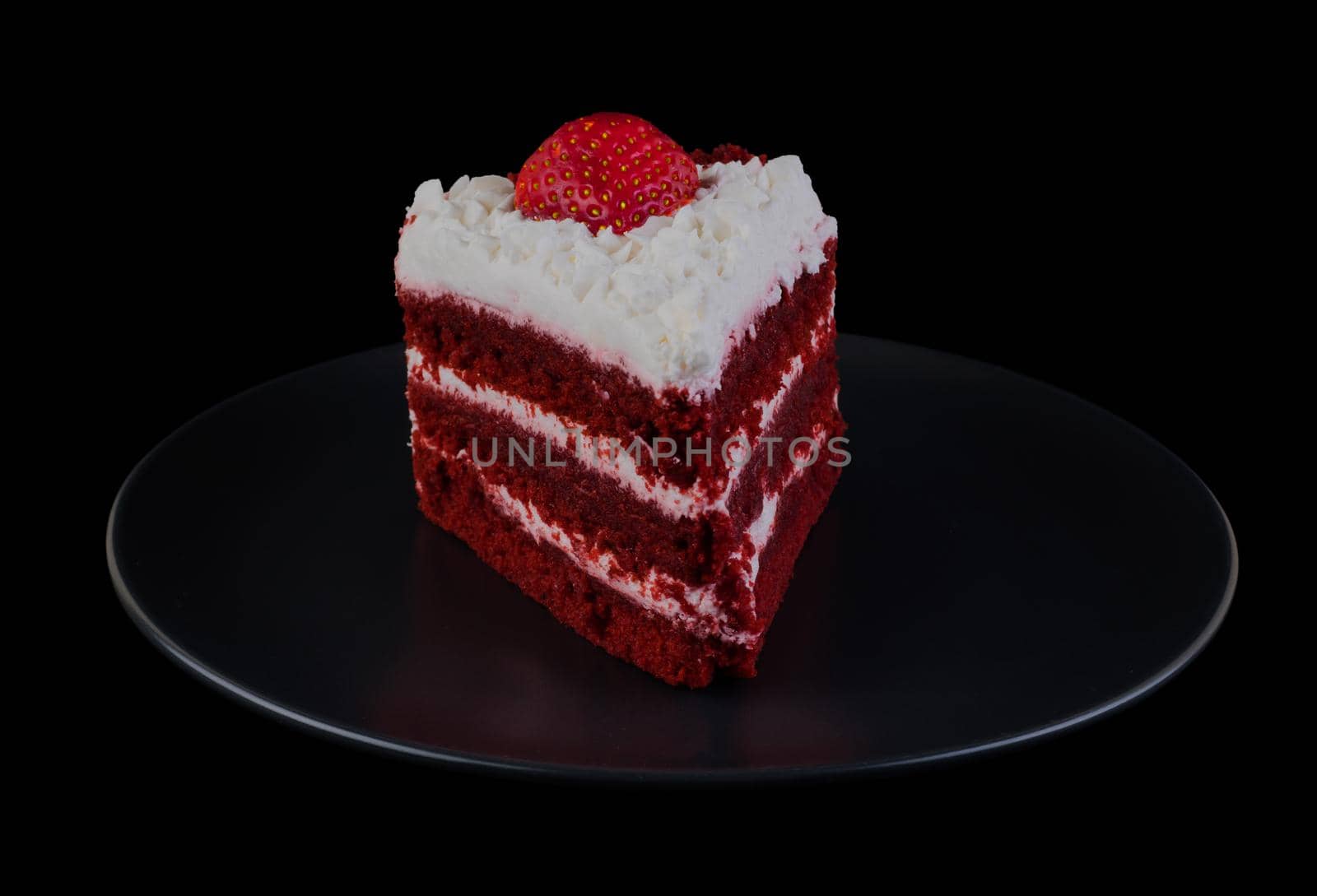 Piece of cake covered with protein cream and strawberries on a black plate and black background