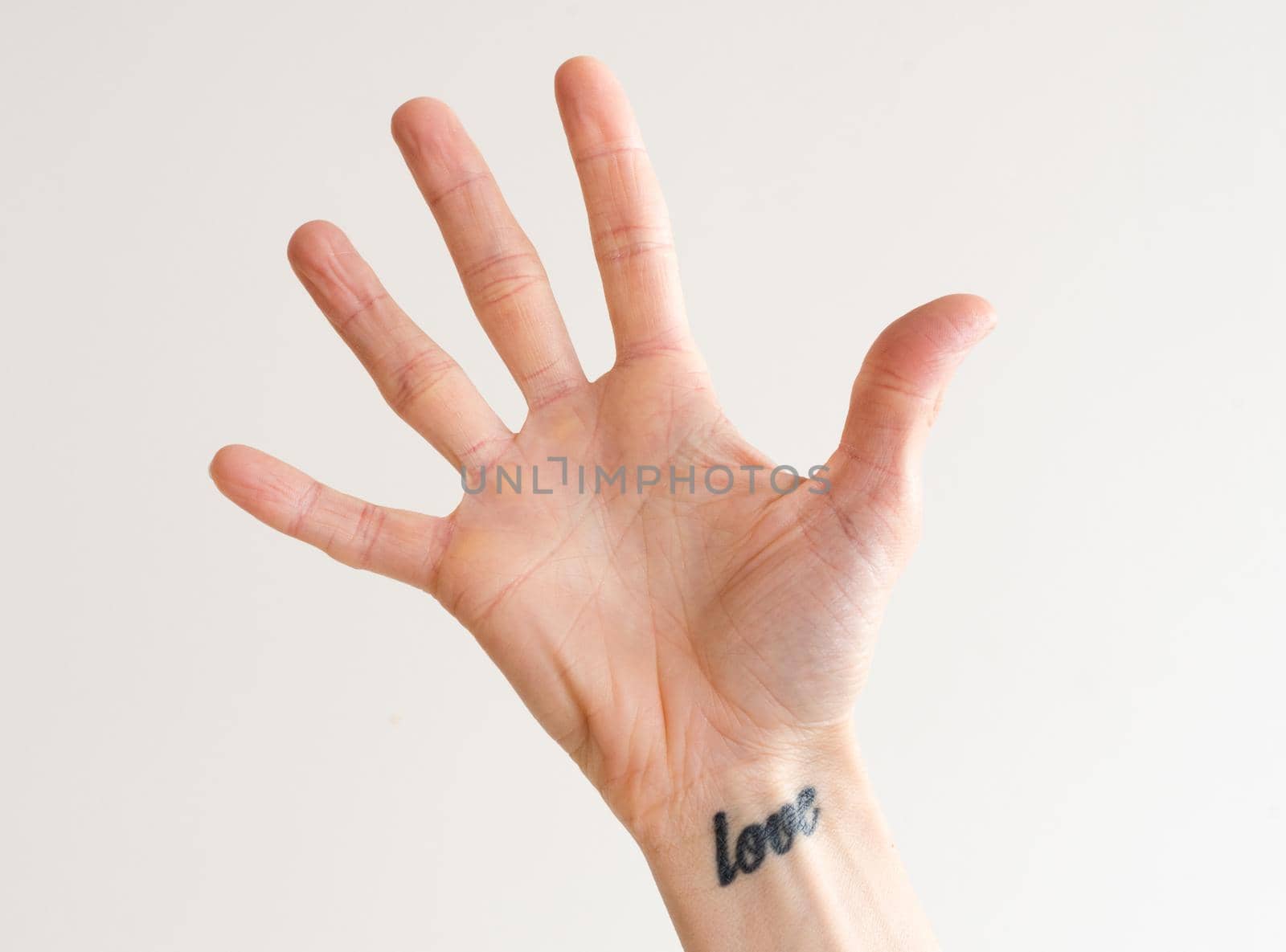 Women's open hand with fingers outstretched and love tattoo on wrist by natalie_board