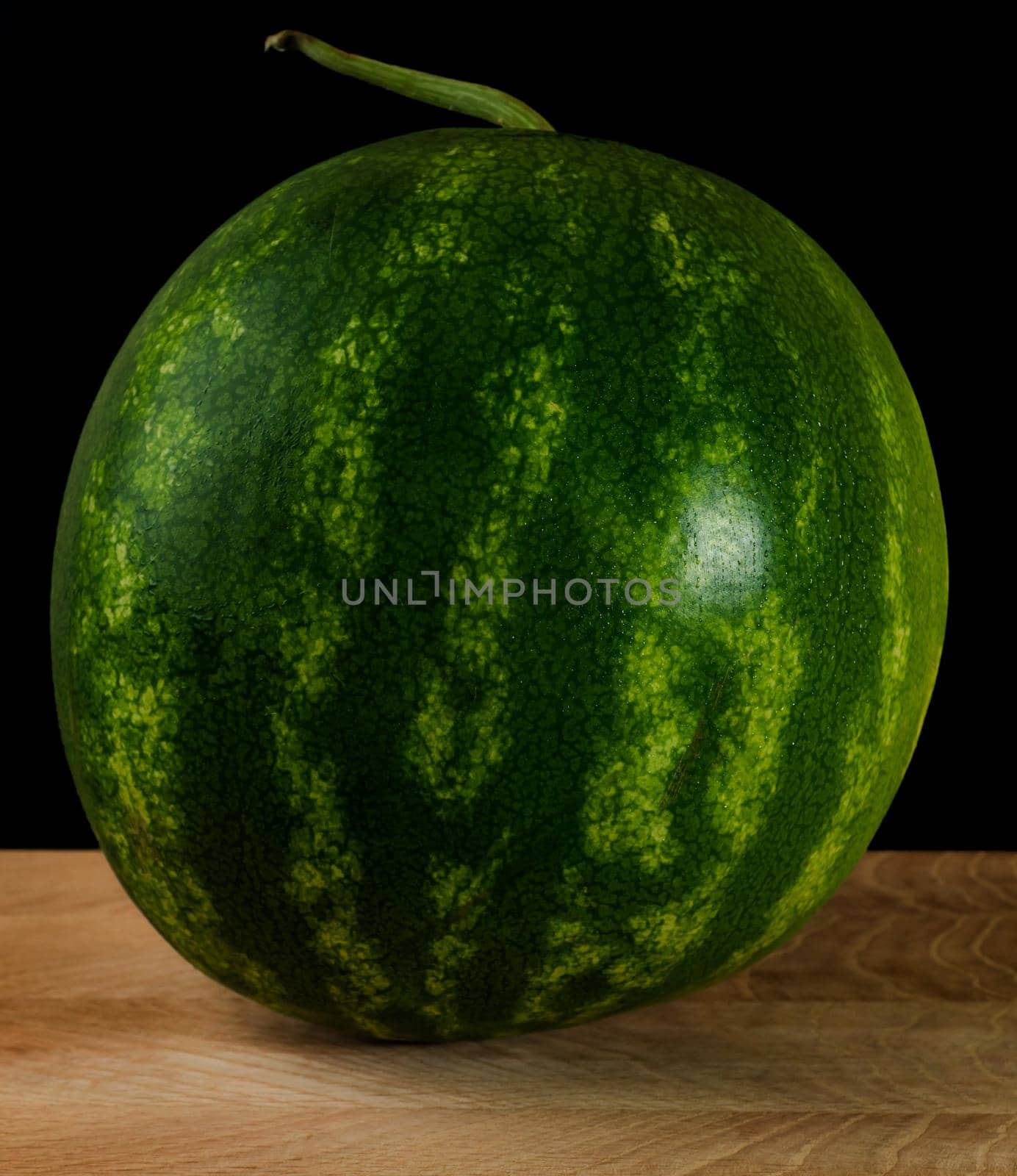 Whole watermelon, on wood board, on black background