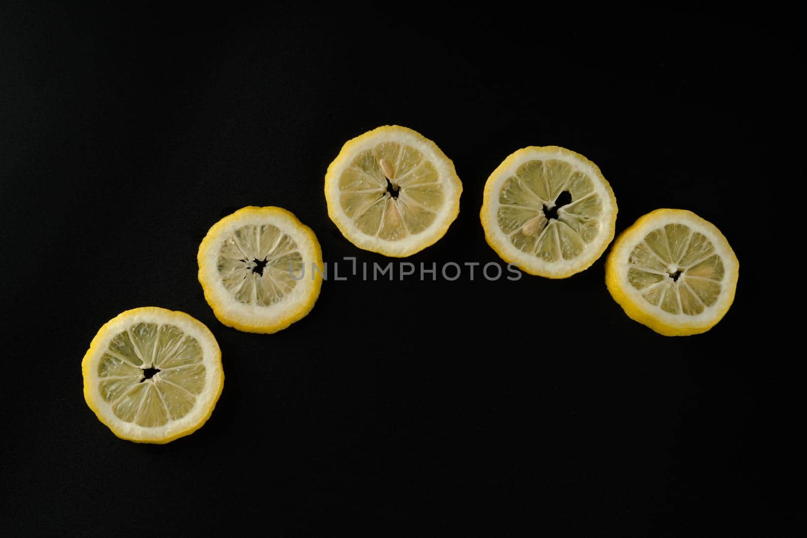 Five lemon slices lined up in a semicircle on a black background isolated by A_A