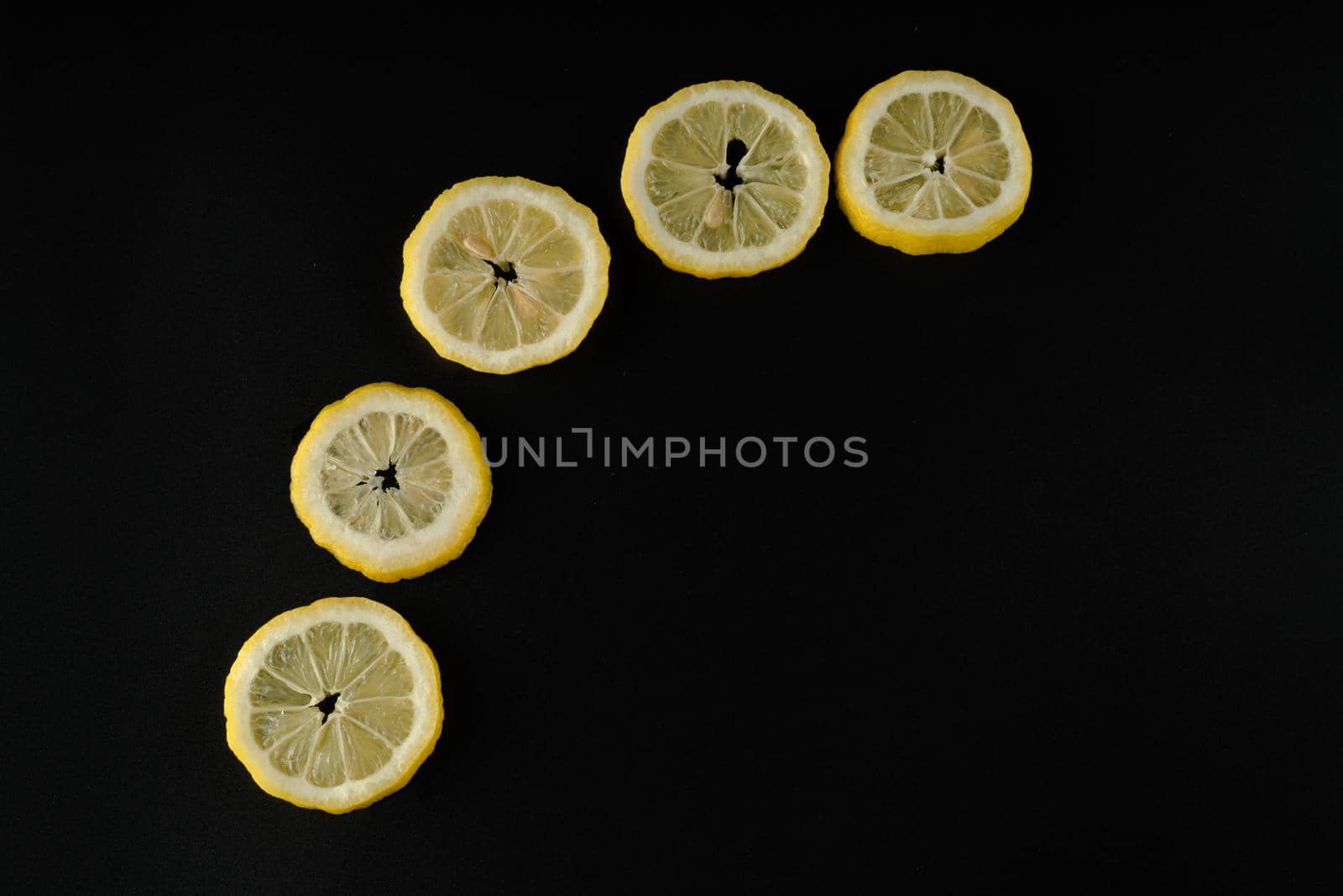 Five lemon slices lined up in a semicircle on a black background