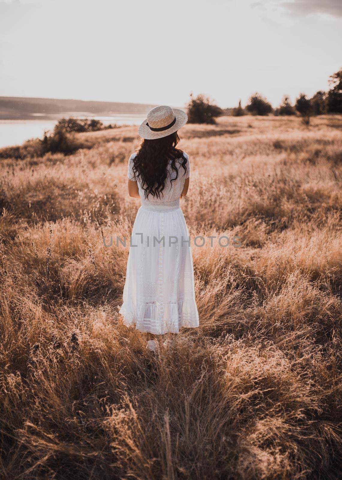 Brunette girl in a white dress with curly hair puts on a boatman hat by AndriiDrachuk