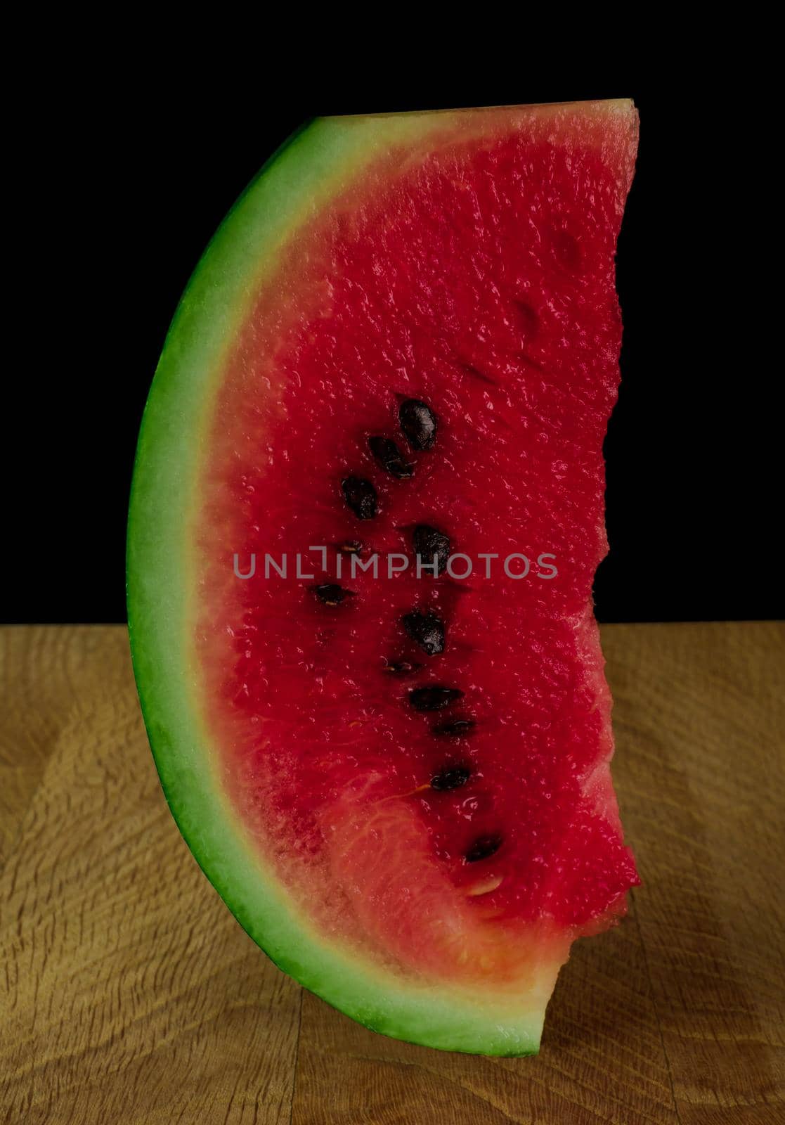 Piece of ripe watermelon, on wood board, on black background