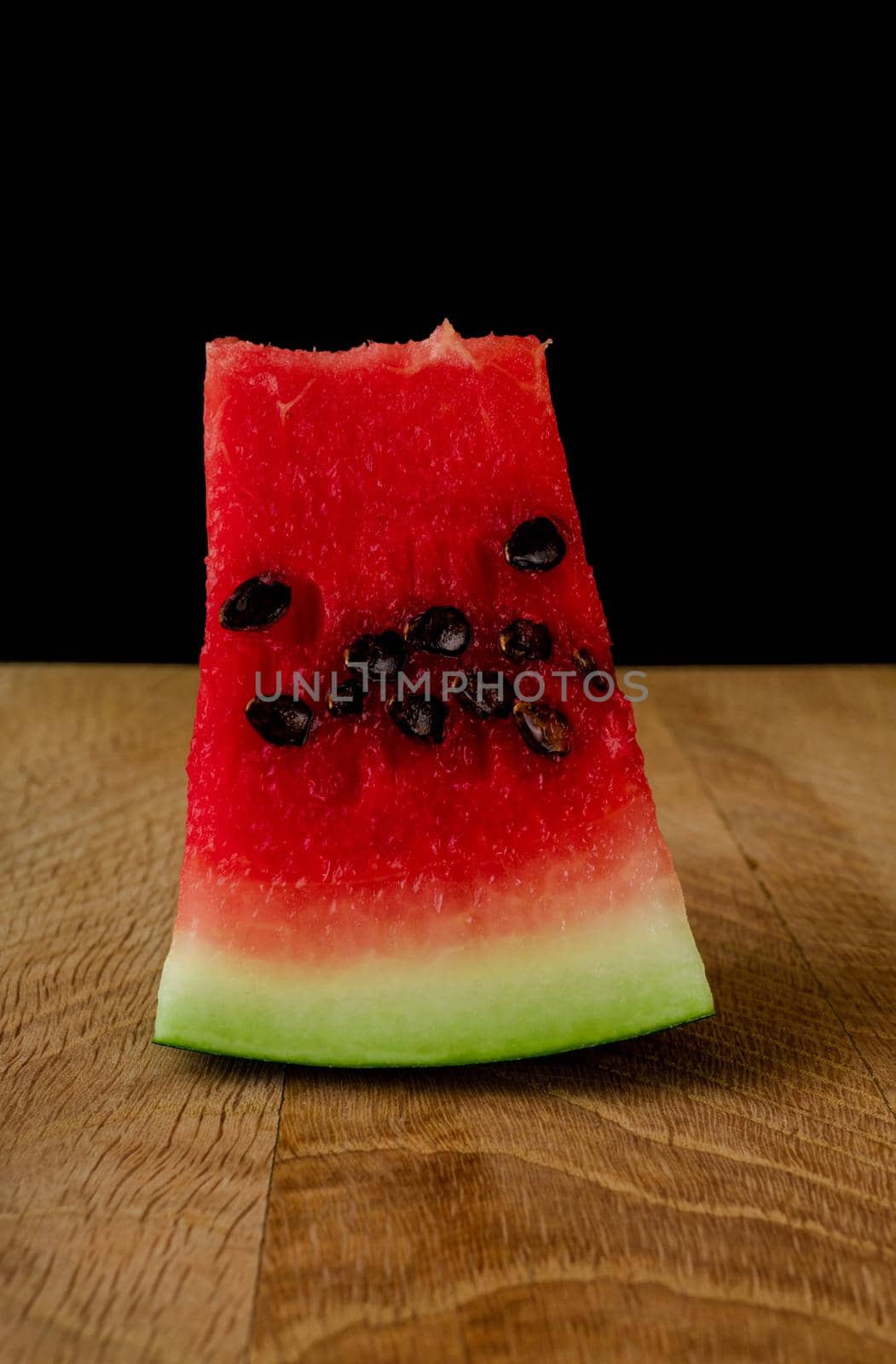 Piece of ripe watermelon, on a wooden board, on a black background