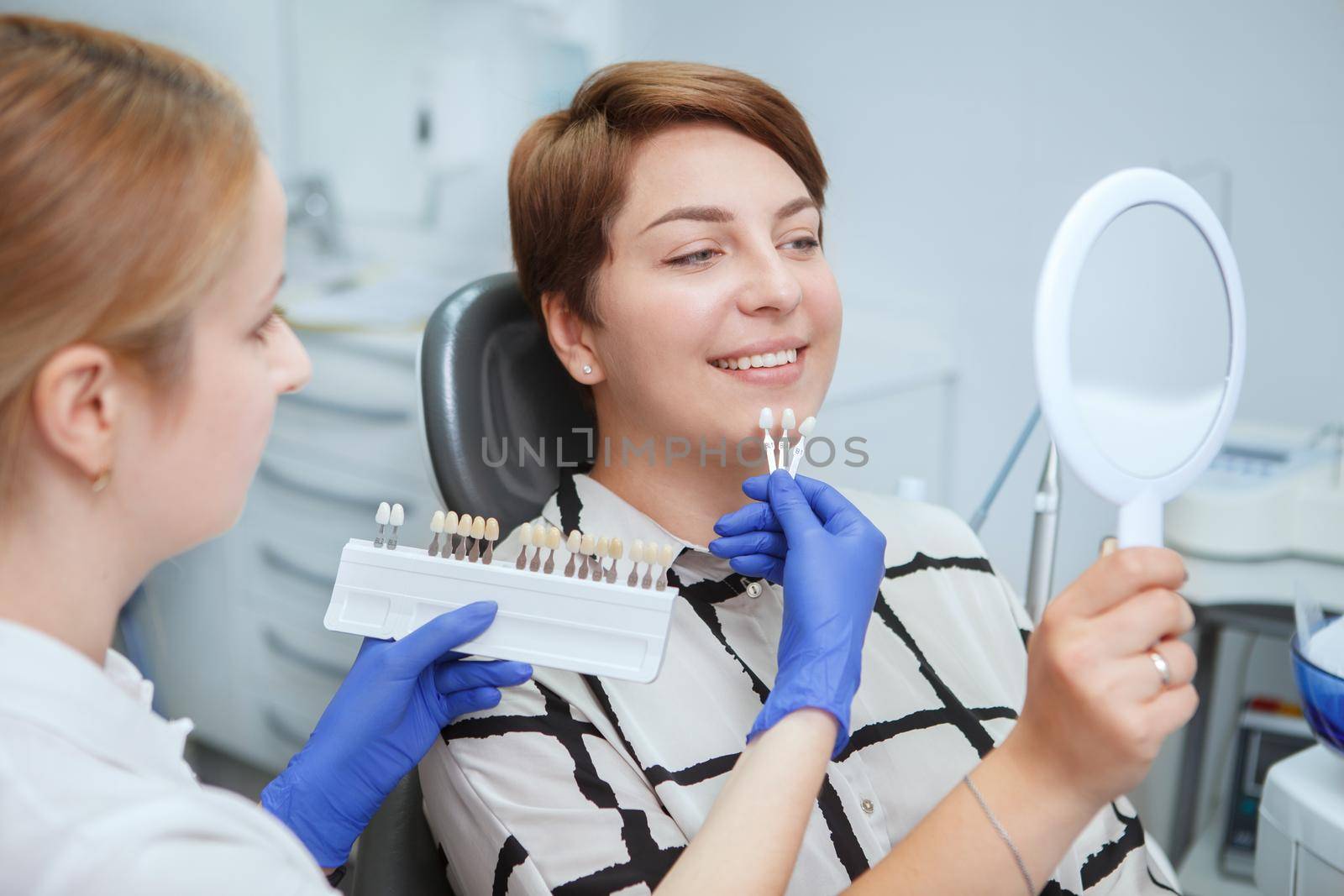 Dentist helping female patient pick teeth whitening shade from the chart