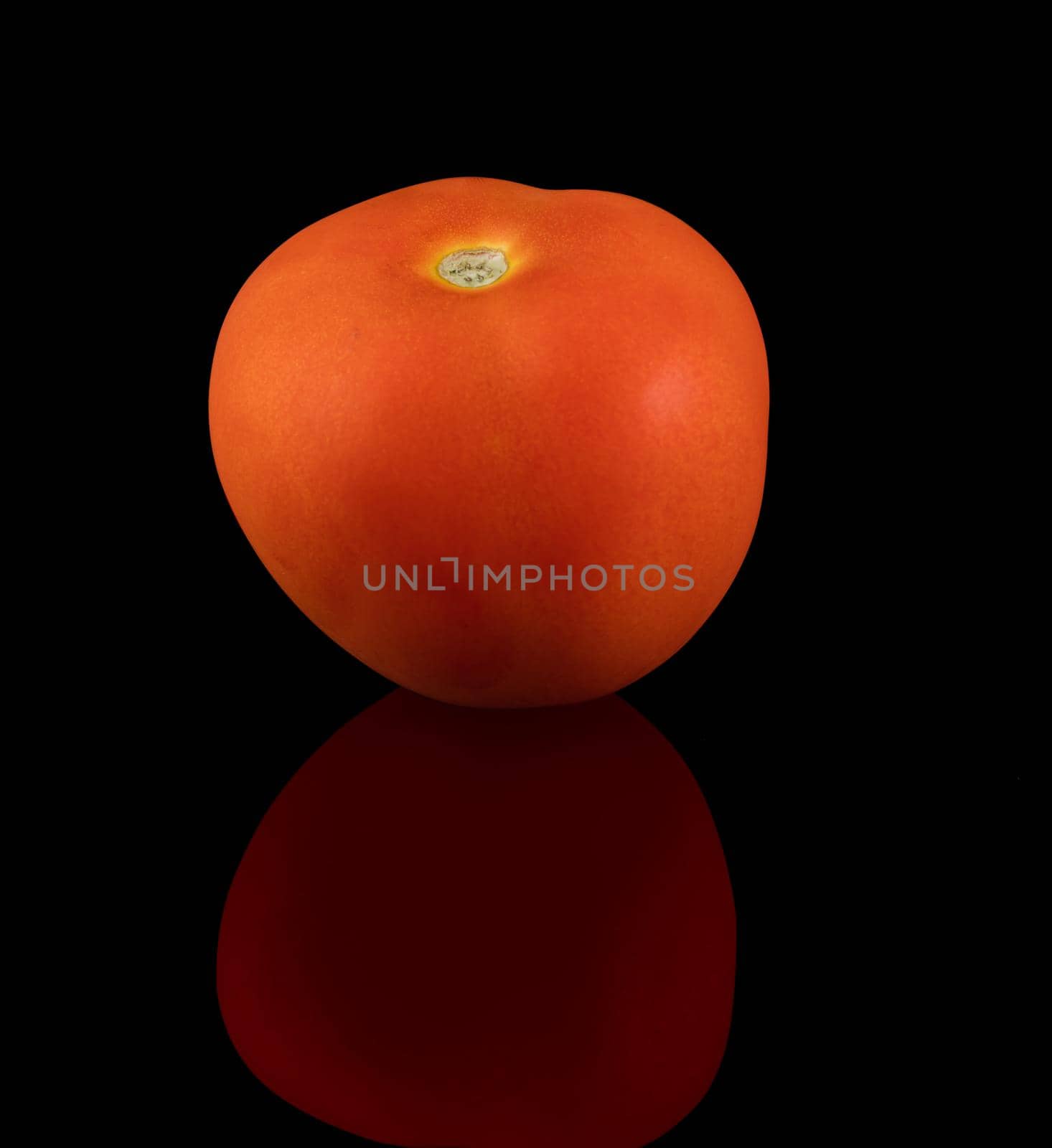 One ripe tomato on a black background, with reflection