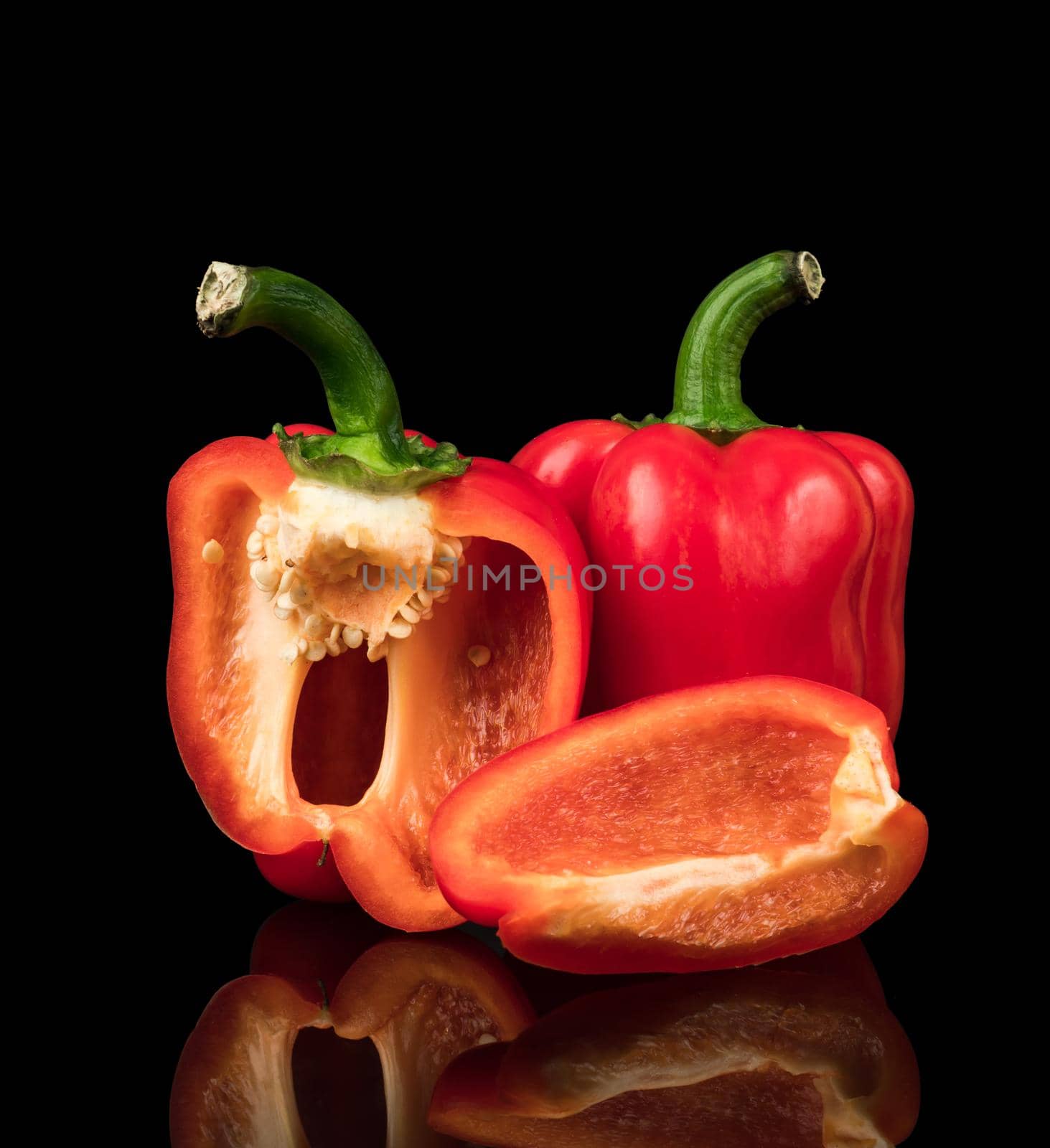 Sweet peppers, red, whole and cut into pieces, on a black background with reflection