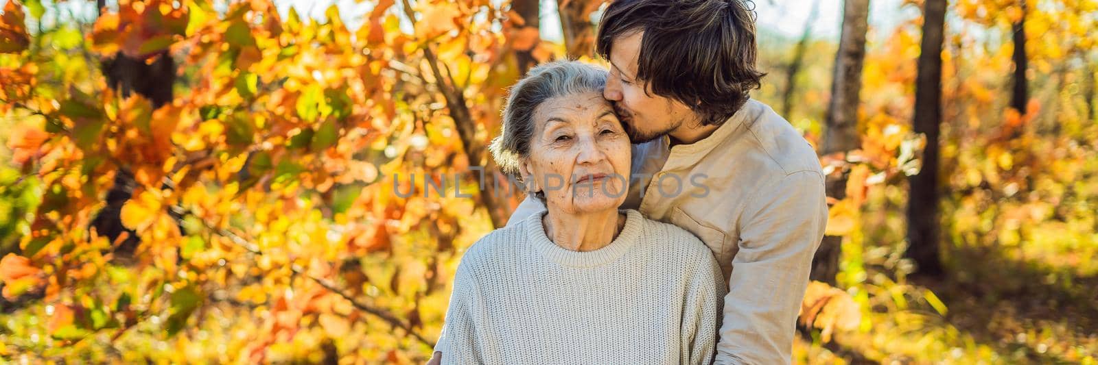 Grandmother and adult grandson hugging in autumn park. BANNER, LONG FORMAT