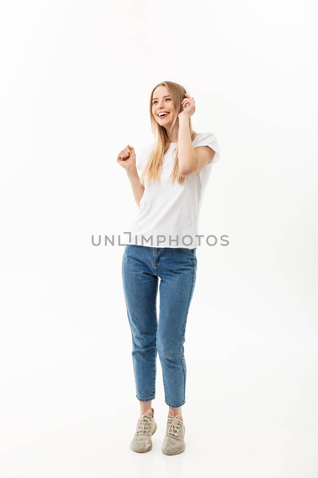 Lifestyle Concept: Portrait of a cheerful happy girl student listening to music with headphones while dancing isolated over white background.