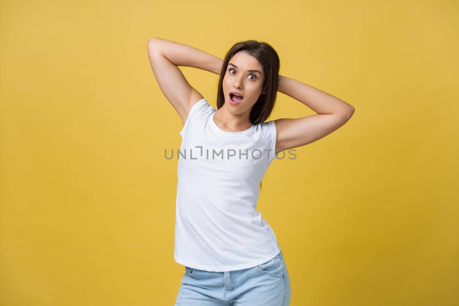 Close-up portrait of cute young woman relaxing with hand behind head. Isolated over yellow background