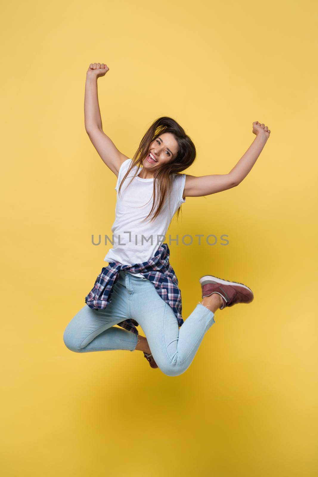 Full length portrait of a cheerful casual caucasian woman jumping isolated over yellow background.