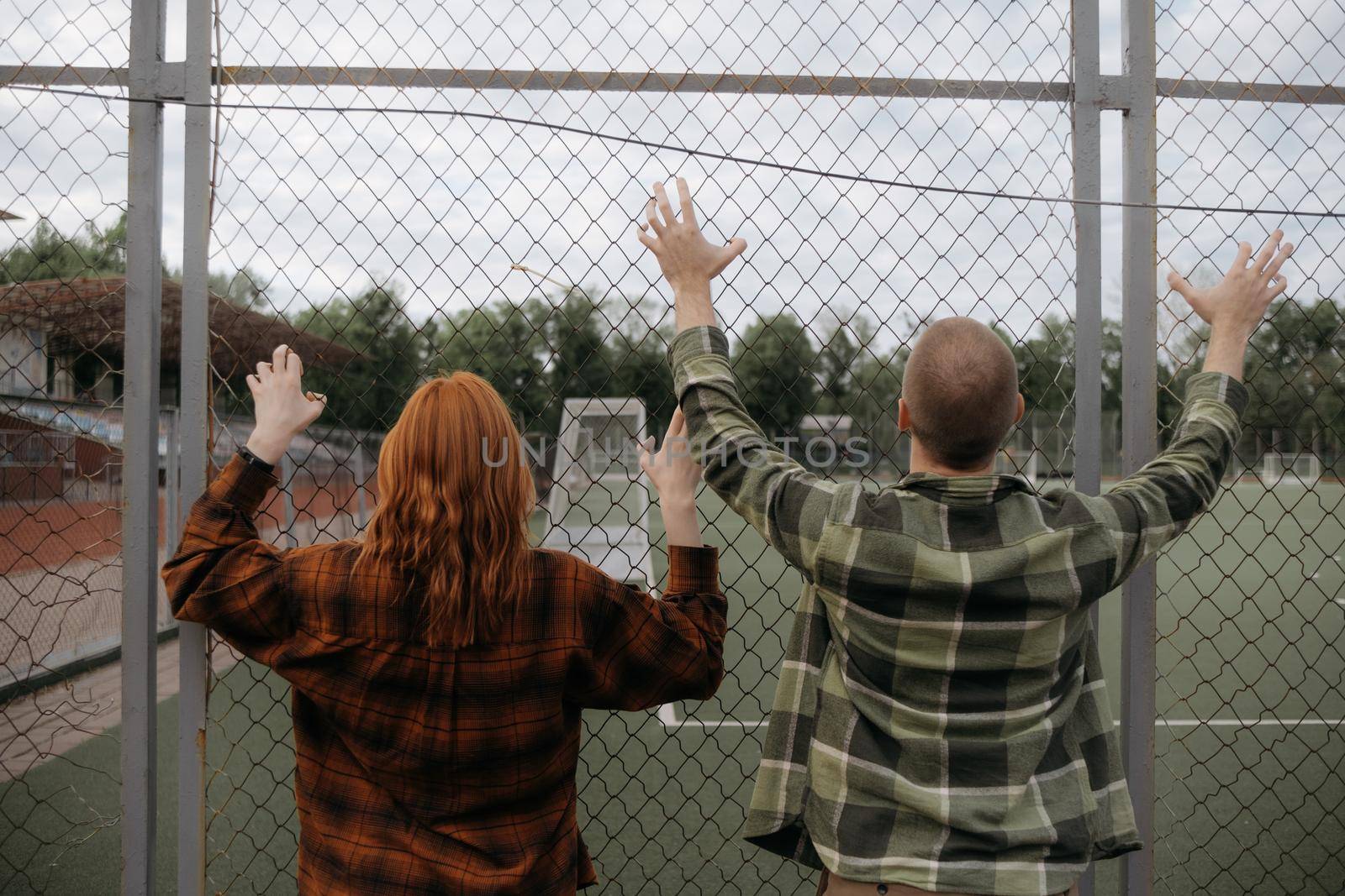 a guy in green and a girl in red stand near the fence and hold on to it with their hands