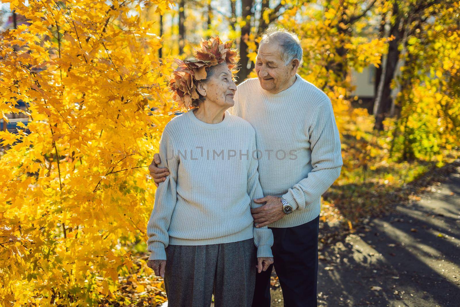 Happy old couple having fun at autumn park. Elderly man wearing a wreath of autumn leaves to his elderly wife.