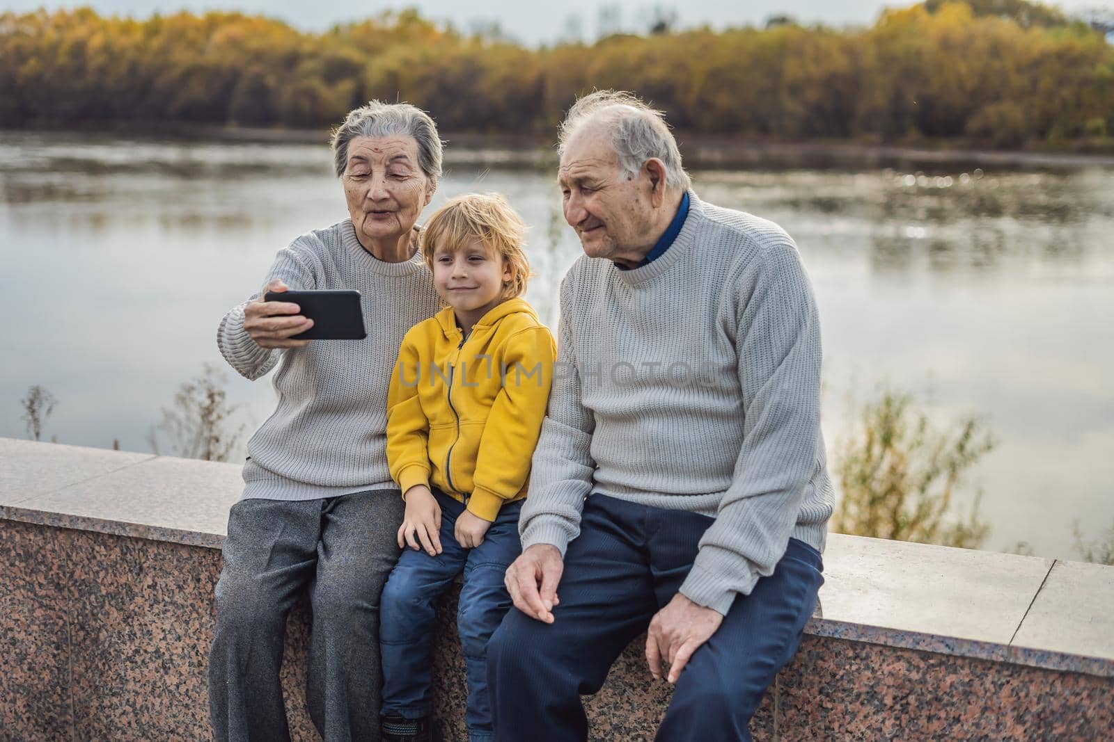 Senior couple with great-grandson take a selfie in the autumn park. Great-grandmother, great-grandfather and great-grandson.