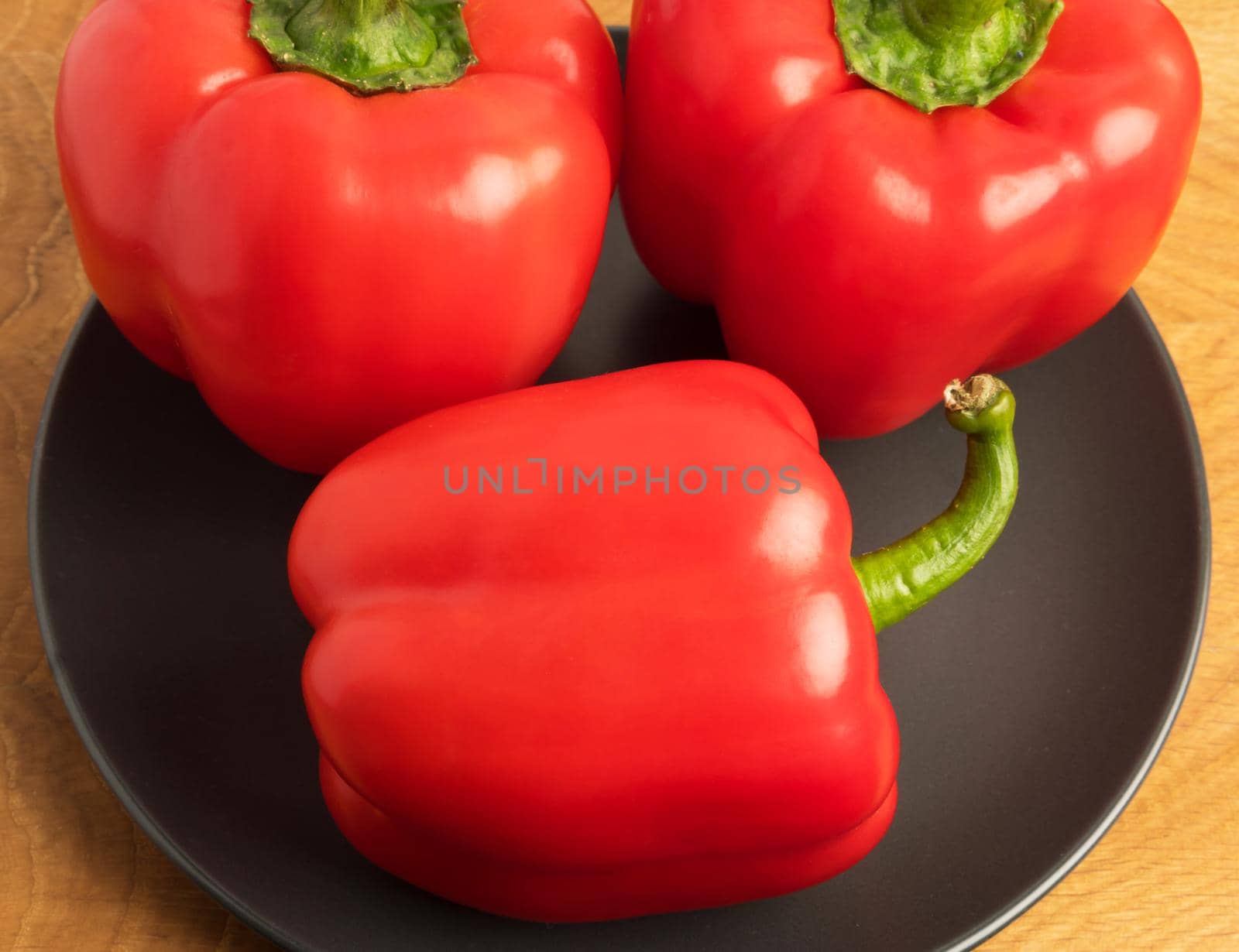 Three sweet red peppers in a black plate on a wooden board