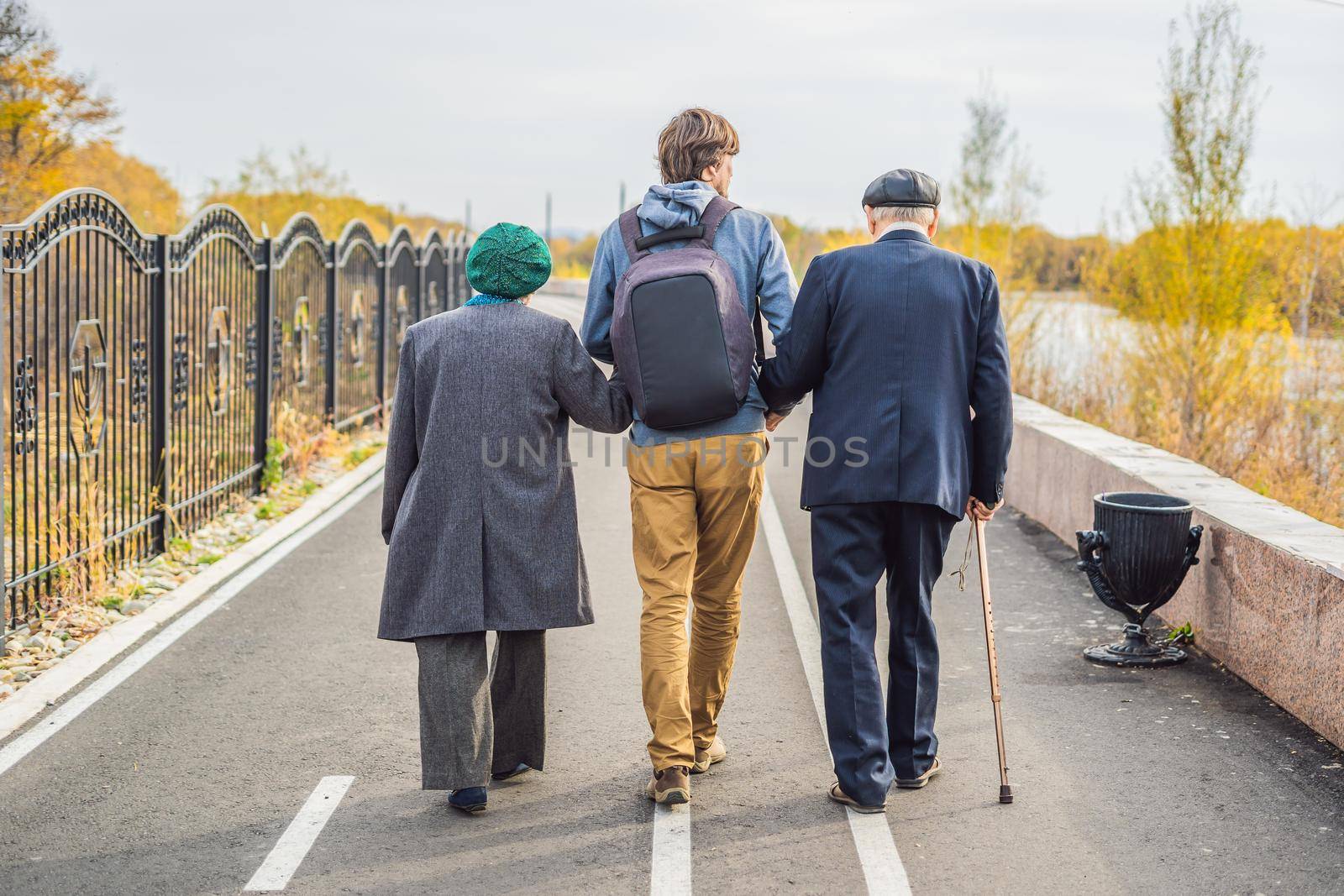 An elderly couple walks in the park with a male assistant or adult grandson. Caring for the elderly, volunteering.