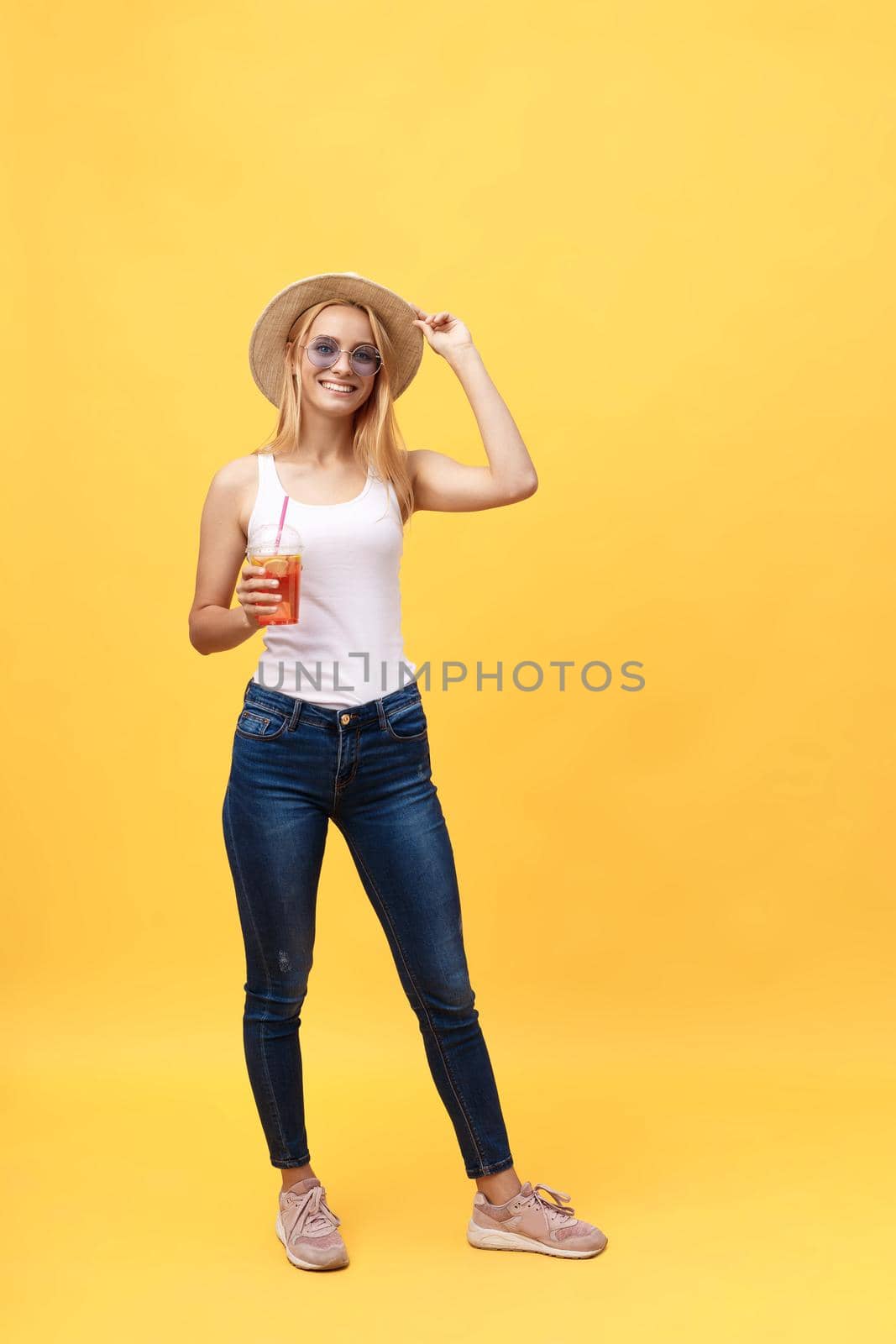 Full length portrait of a cheerful young woman wearing summer clothes while posing and looking at camera isolated over yellow summer background.