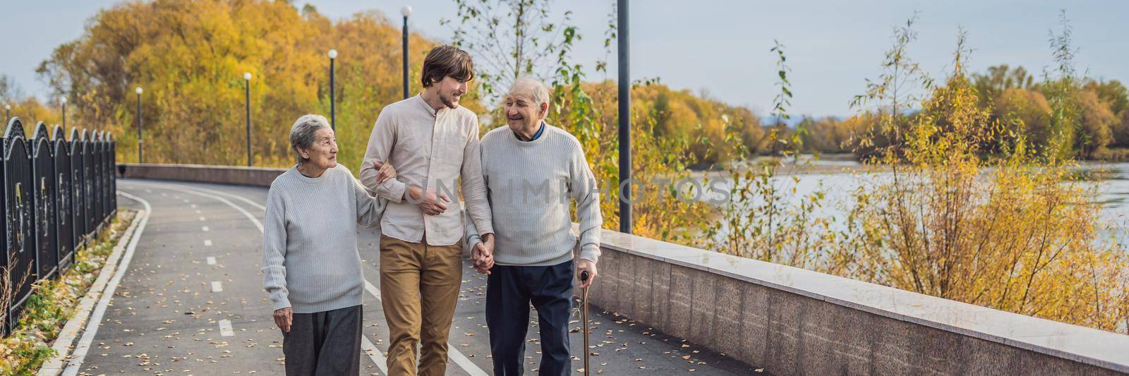 BANNER, LONG FORMAT An elderly couple walks in the park with a male assistant or adult grandson. Caring for the elderly, volunteering.