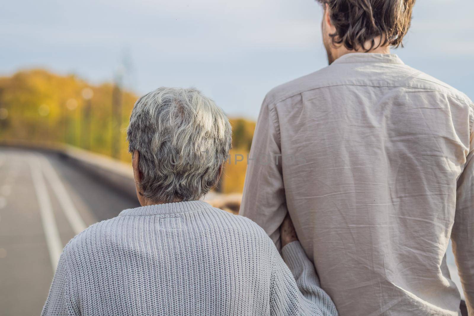 An elderly couple walks in the park with a male assistant or adult grandson. Caring for the elderly, volunteering.